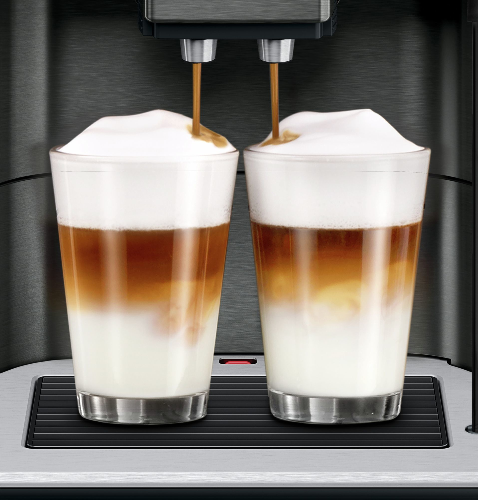 Dwie szklanki latte wlewane przez maszynę. Latte składa się z mleka, kawy i piany.