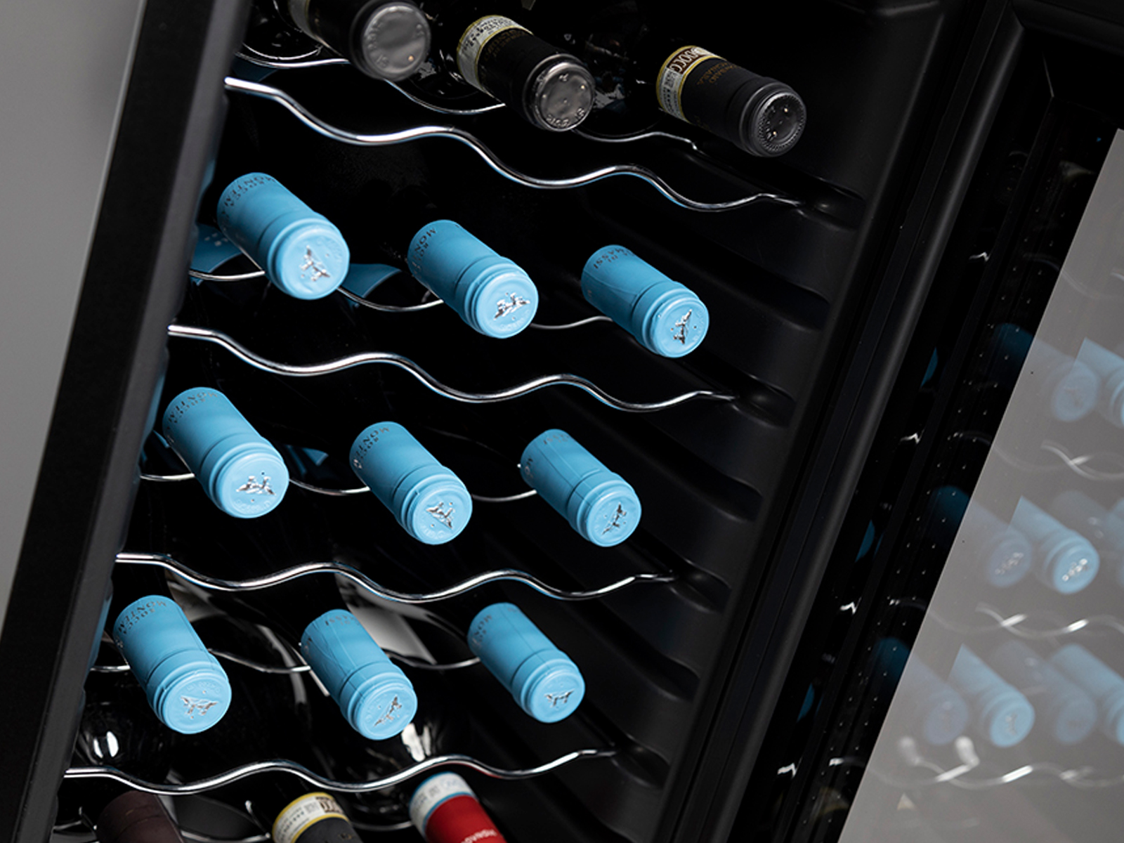 Botellas de vino almacenadas en una vinoteca negra, con etiquetas de tapa azul visibles.