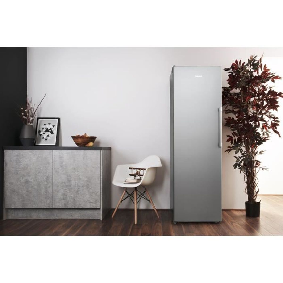 Kühlschrank in einem Raum, neben einer Pflanze, einem Schrank und einem Stuhl.