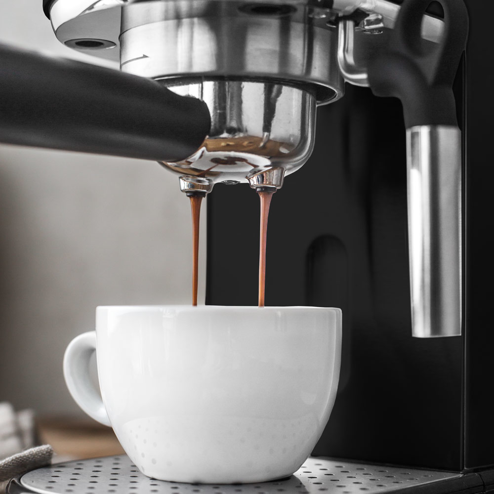 Kawa wylewająca się z ekspresu do espresso do białego kubka.