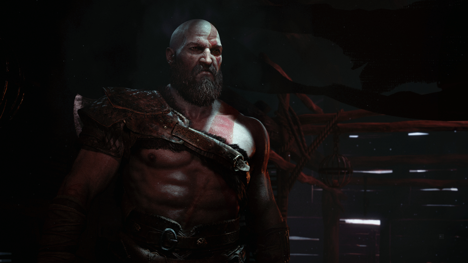 Kratos z God of War, bez koszulki, z brodą, patrzący w bok w słabo oświetlonym pomieszczeniu.