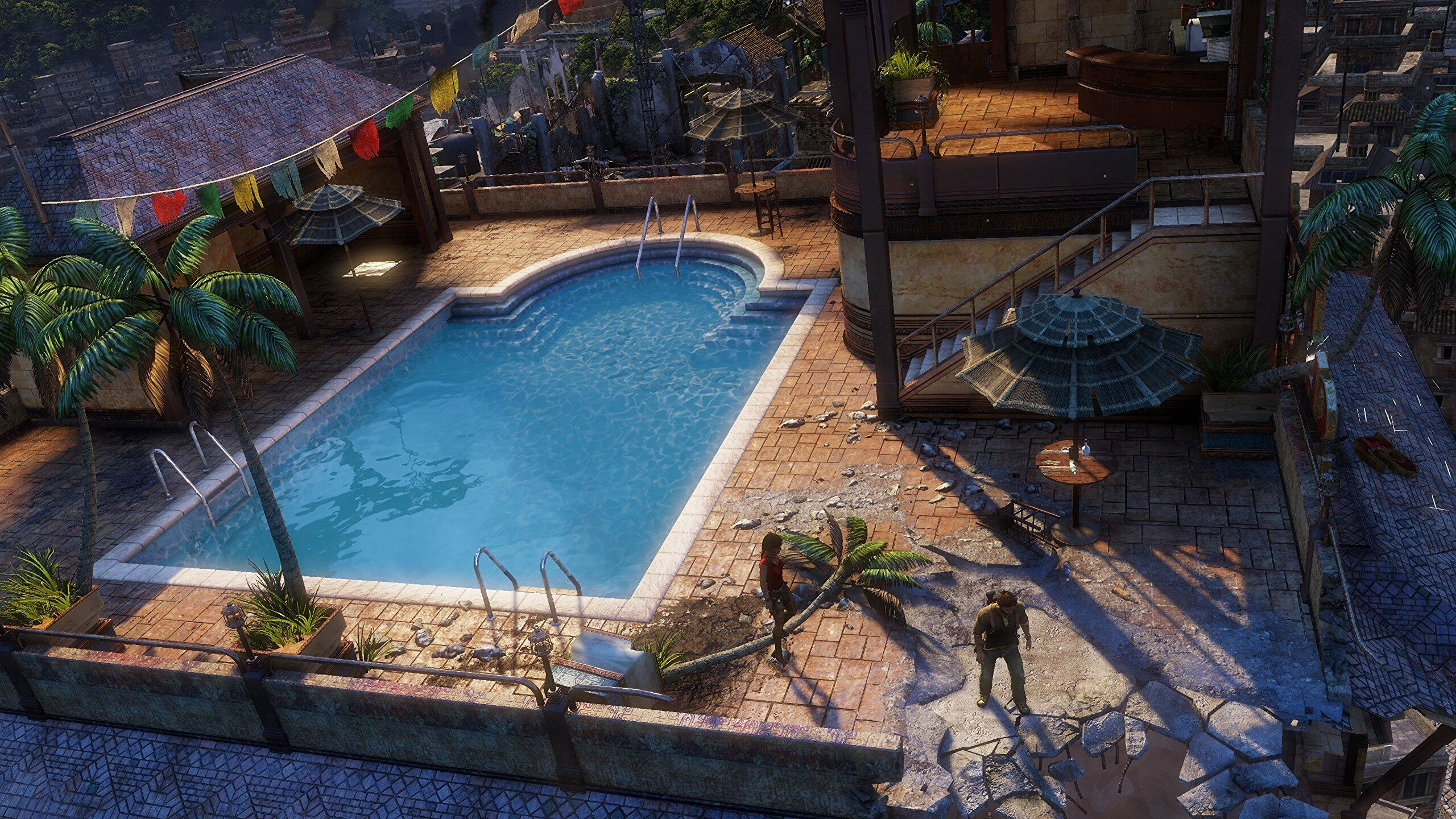 Eine Vogelperspektive auf einen Pool mit Menschen, Gebäuden und Palmen in tropischer Umgebung.