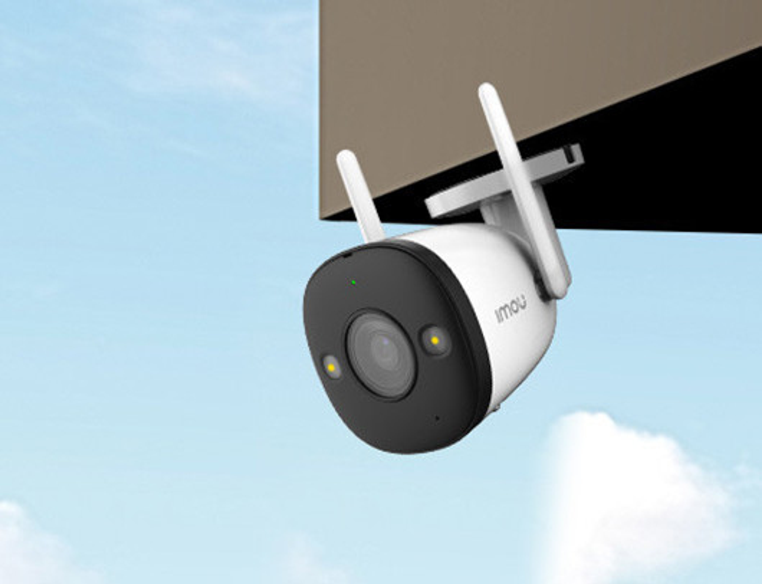 White and black security camera, mounted under a brown structure, against a blue sky.