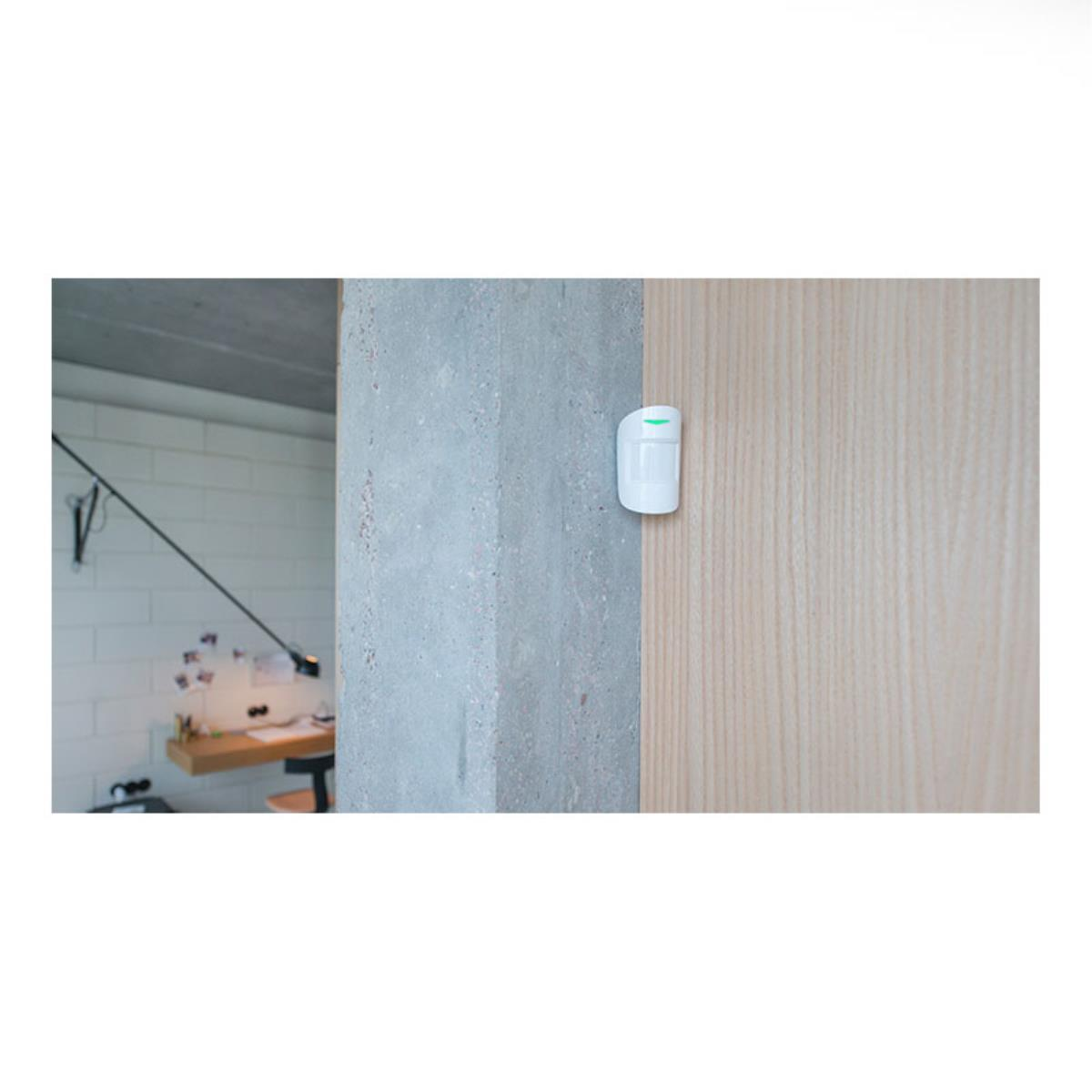 Sensore di movimento bianco montato su pilastro di cemento e porta in legno.