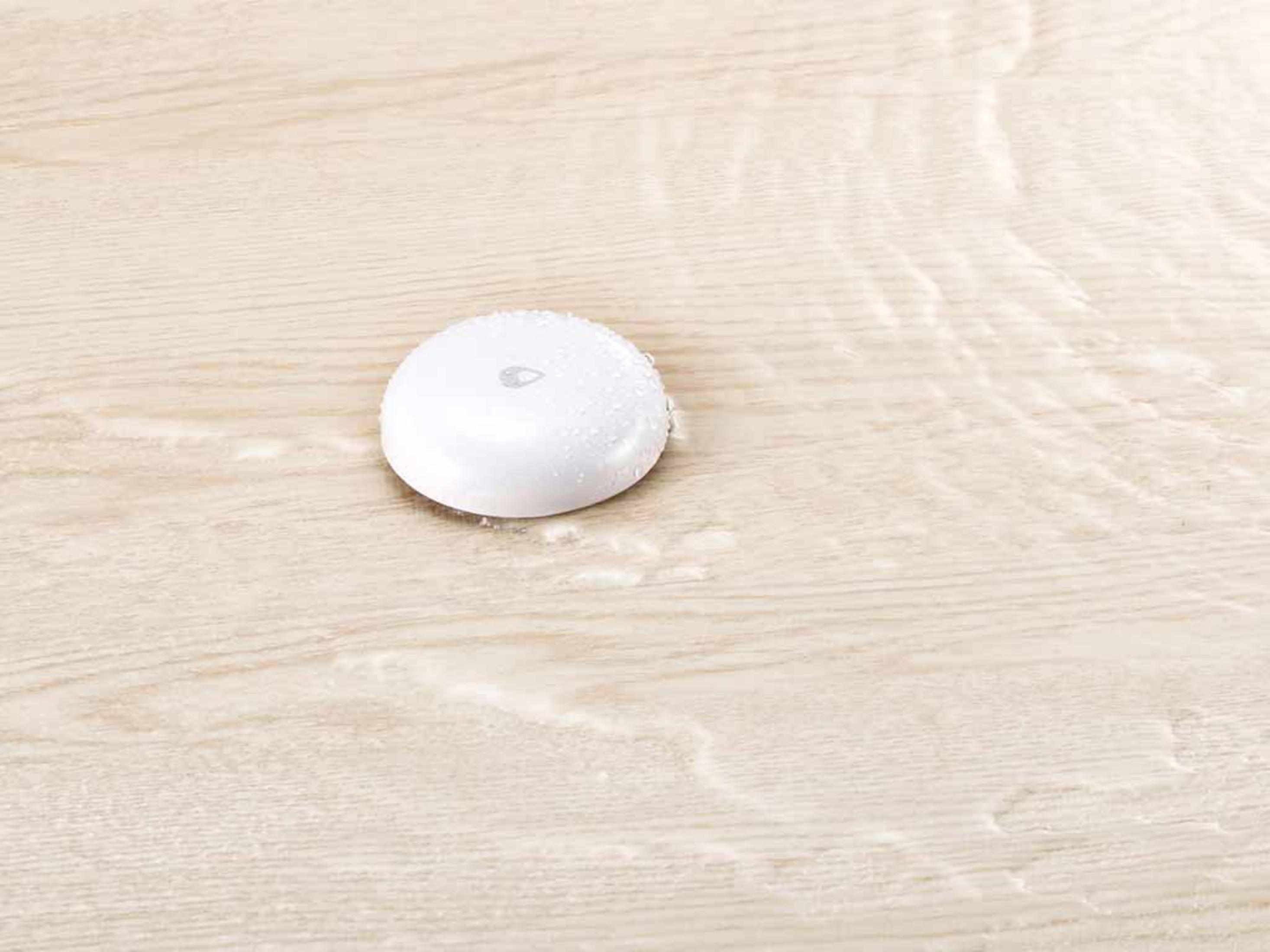 Biały czujnik wody na drewnie. Woda otacza urządzenie.