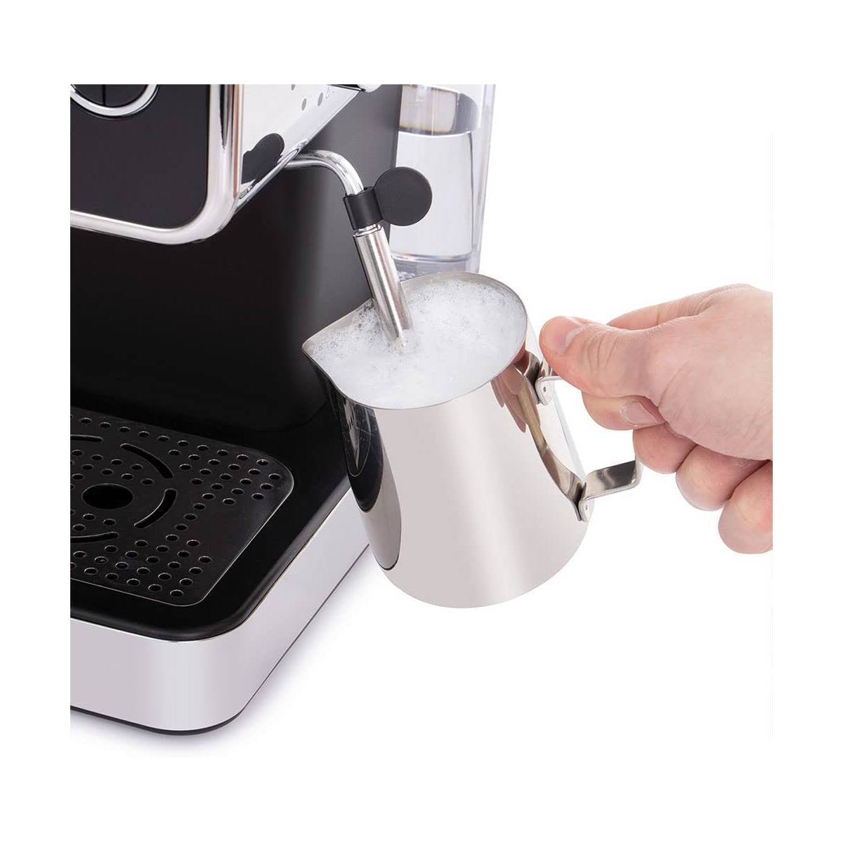 Bir el çelik bir sürahi ile süt köpürtüyor. Arka planda espresso makinesi. Köpük görünür.