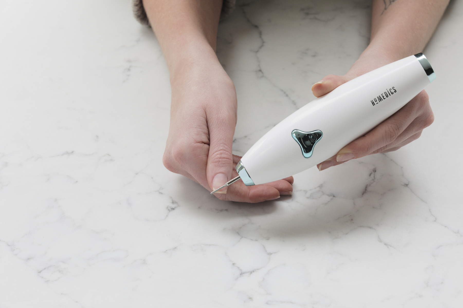 Dłonie trzymające urządzenie do pielęgnacji paznokci nad marmurową powierzchnią.