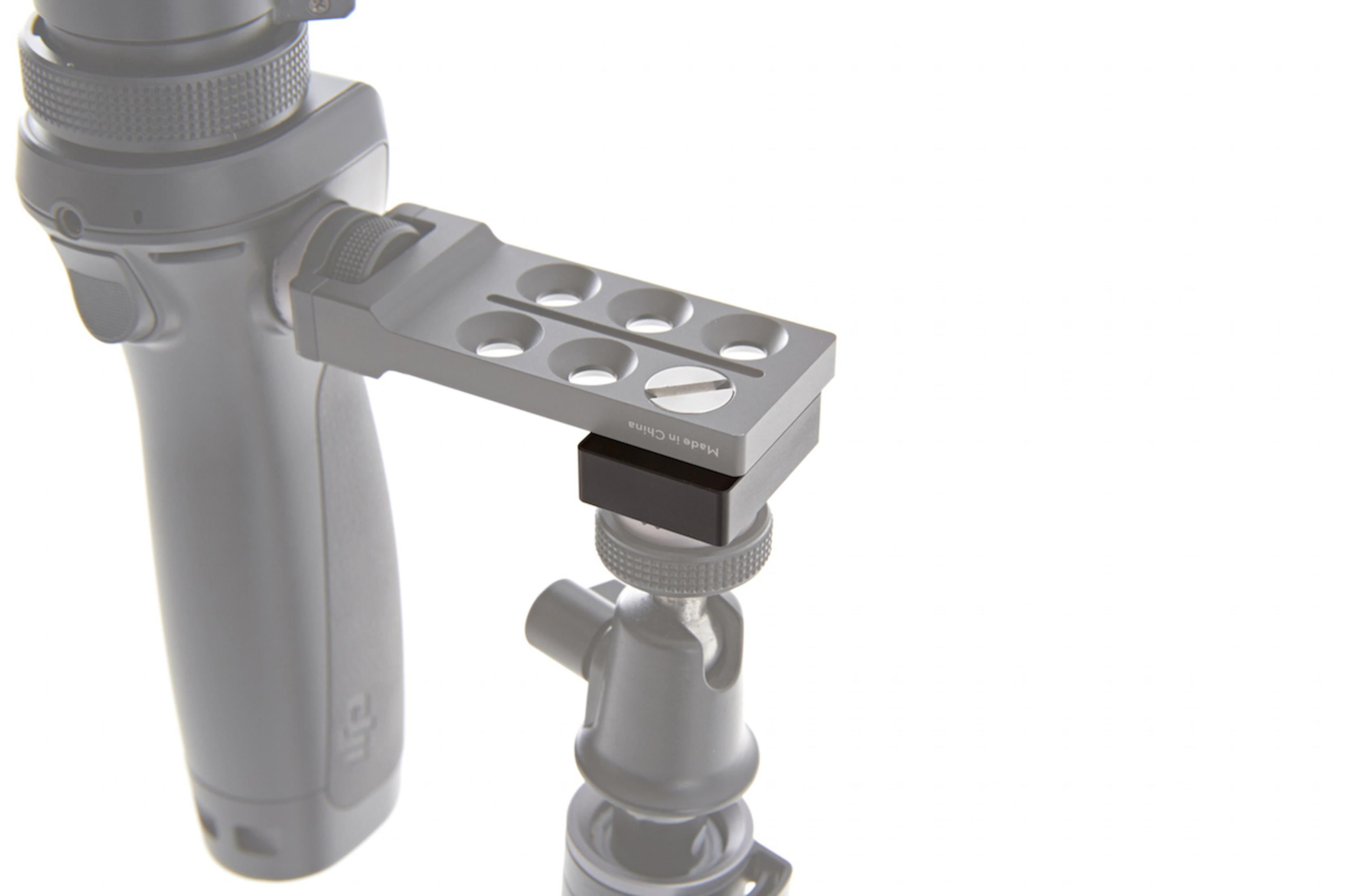 Uno stabilizzatore per fotocamera grigio con un pezzo di collegamento nero, montato su un treppiede, sfondo bianco.