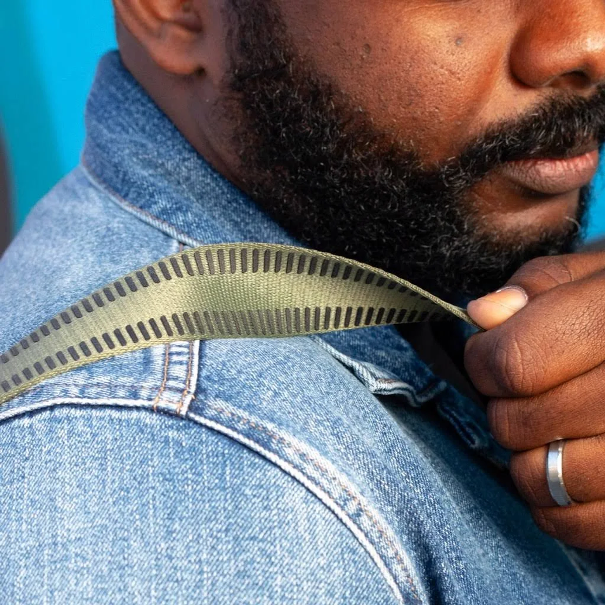 Zbliżenie dłoni mężczyzny regulującej zielony pasek do aparatu. Jeansowa kurtka.