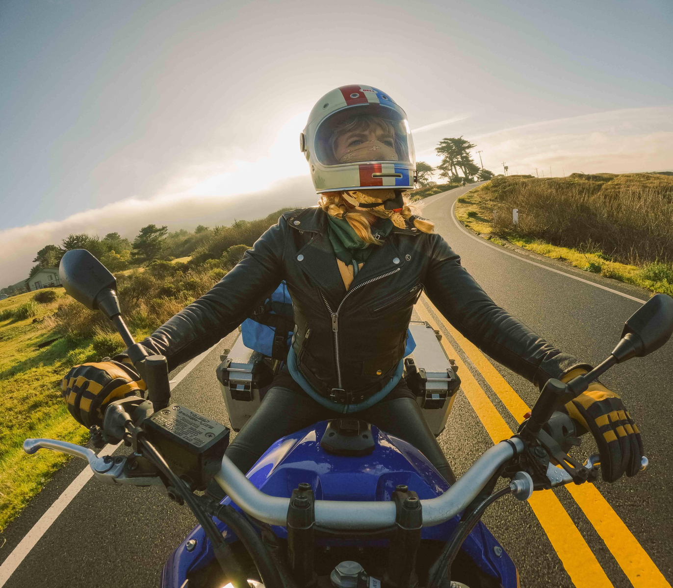 Kobieta jadąca motocyklem po drodze, w kasku i ekwipunku.