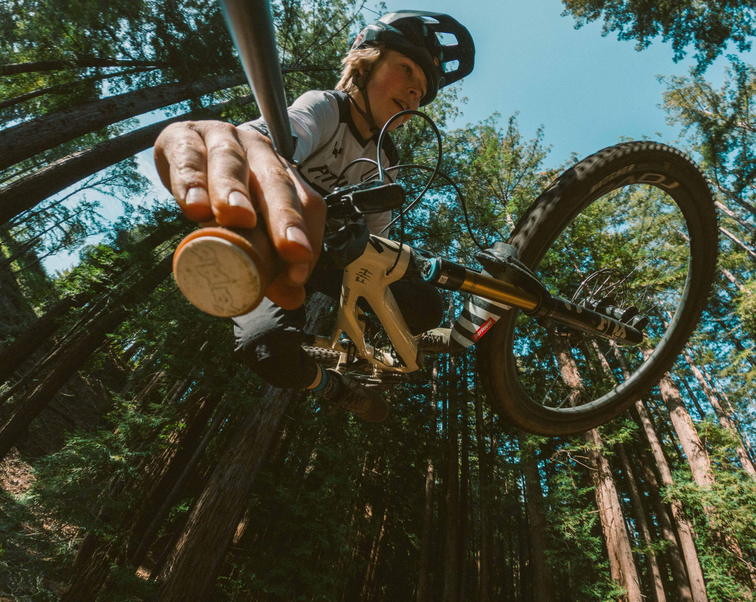 Kolarz górski w powietrzu, skaczący, drzewa w tle. Widoczne niebo i las.