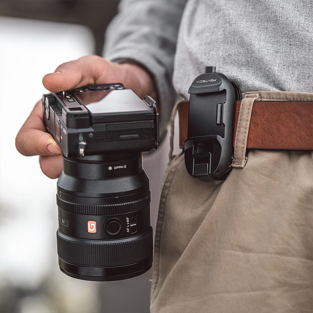 Osoba trzymająca aparat. Aparat jest przymocowany do klipsa na pasku w talii.