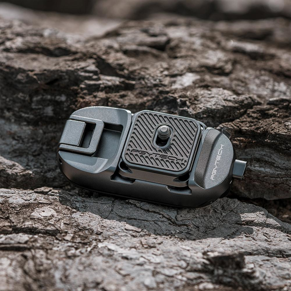 Szary uchwyt do aparatu na skałach, z czarną płytą i srebrnym pokrętłem, otoczenie zewnętrzne.