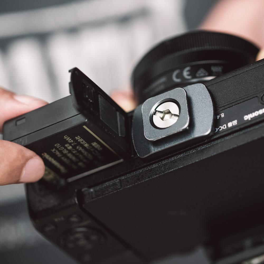 Ręka wkładająca baterię do aparatu obok zamontowanej płytki.