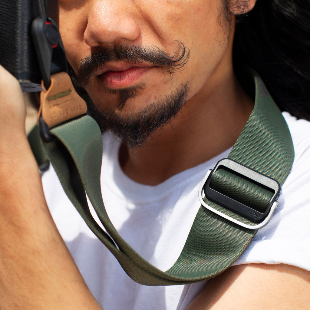 Mężczyzna z paskiem od aparatu na szyi. Pasek jest zielono-czarny. Ma na sobie białą koszulę.