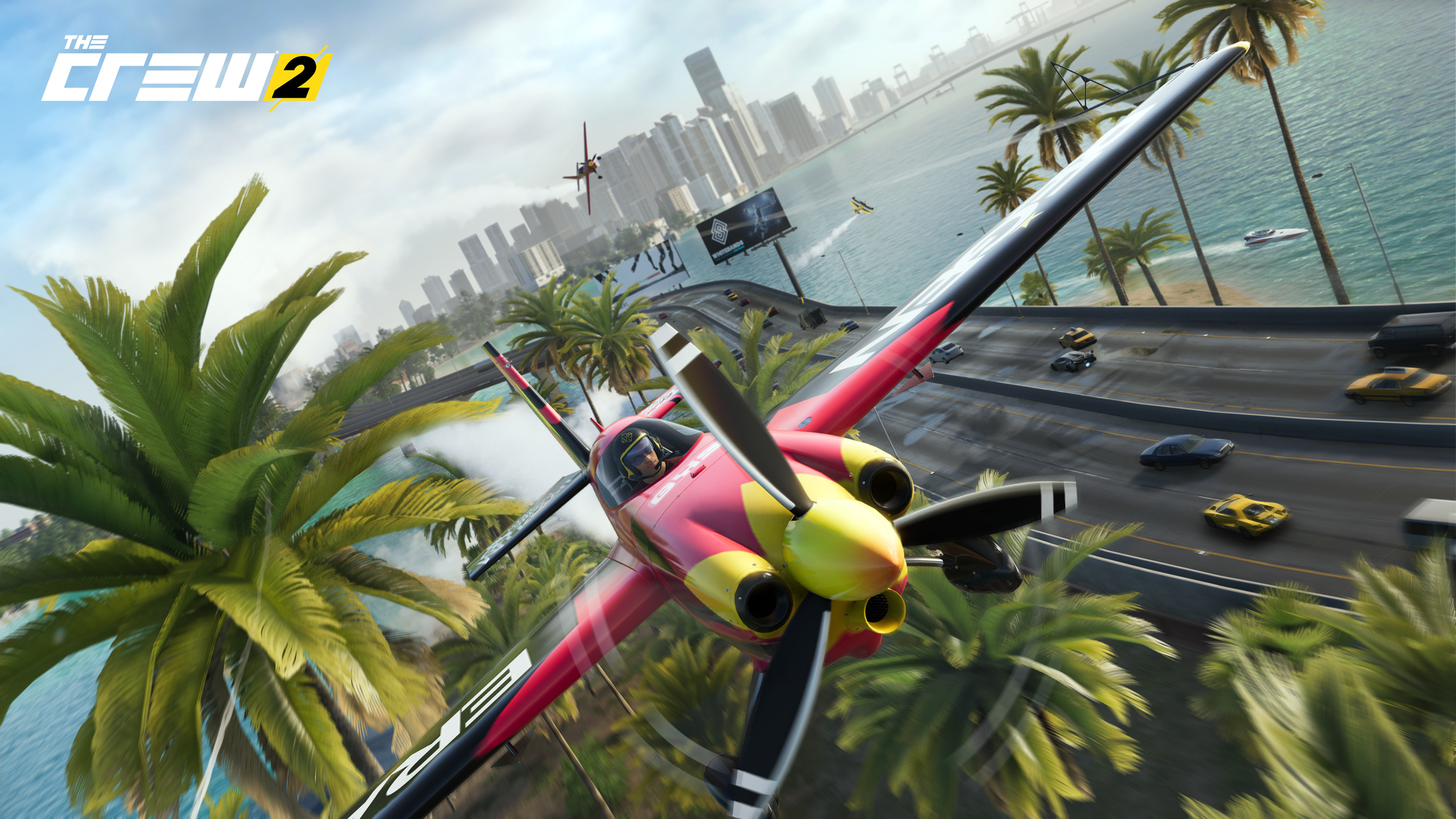 Scena z gry The Crew 2. Samolot lecący nad nadmorskim miastem z palmami, łodziami i innymi pojazdami.