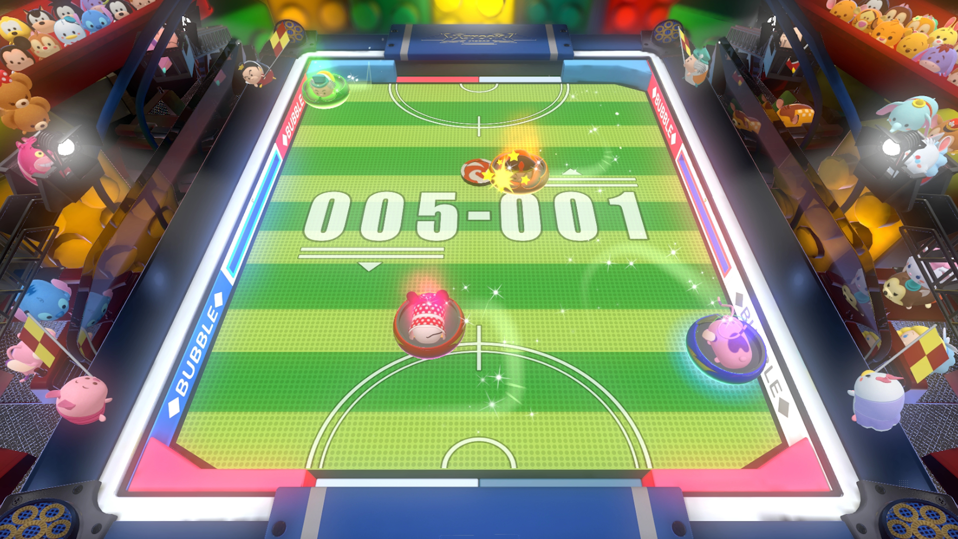 Ekran gry z tablicą wyników i postaciami na arenie w kształcie bąbelka grającymi w grę.