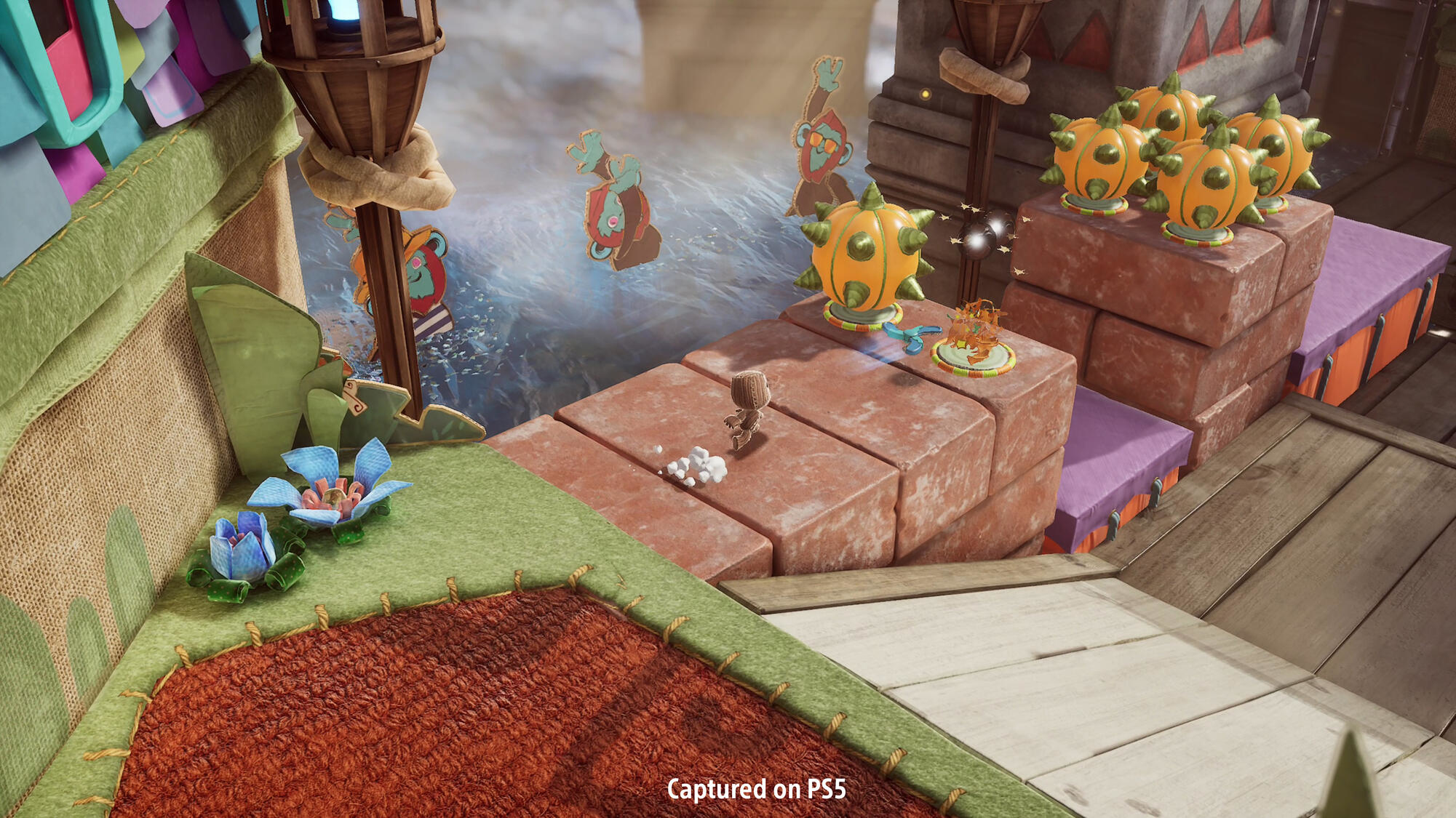 Mała postać idzie ścieżką. Obecne są dekoracyjne obiekty i drewniana platforma.