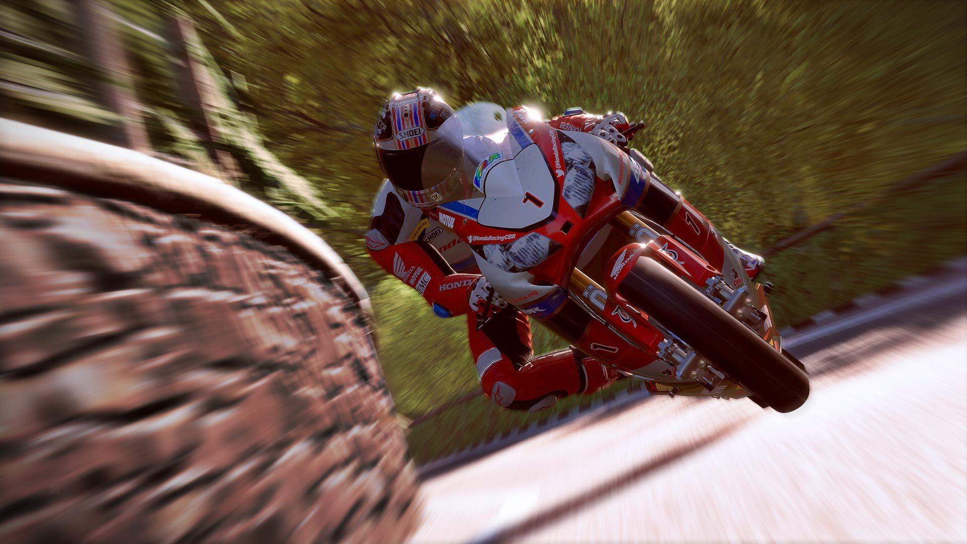 Corsa motociclistica su strada, pilota con equipaggiamento rosso e bianco, sfondo sfocato di strada e alberi.