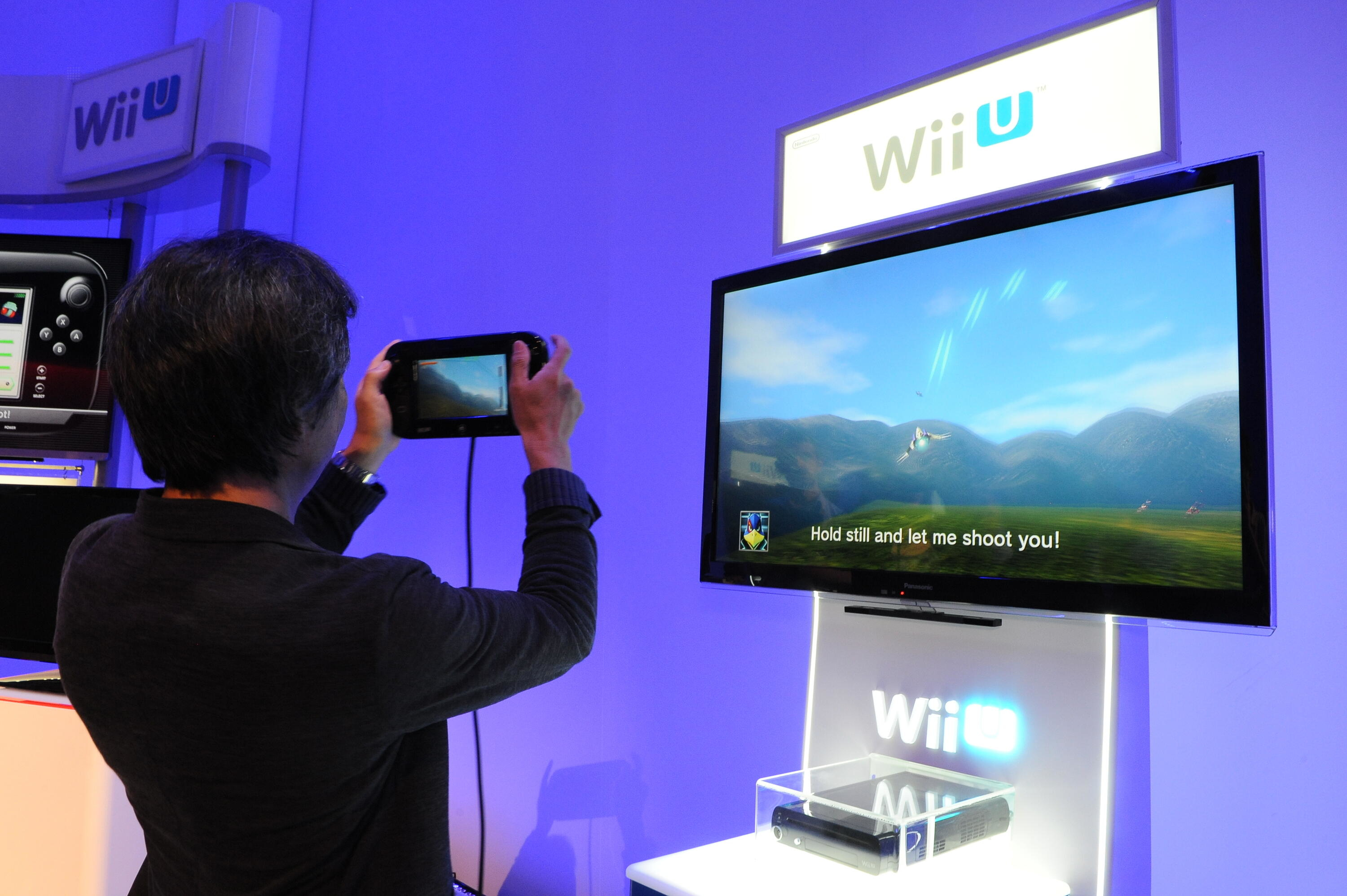 Eine Frau, die ein Wii U Gamepad hält und auf einen Fernsehbildschirm mit einem Spiel blickt.