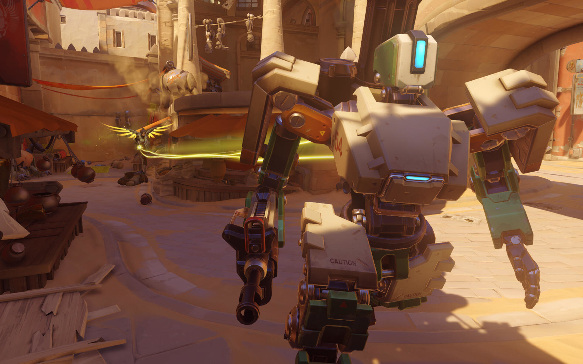 Scena z gry Overwatch. Robot z bronią stojący na zewnętrznym targu z żółtym światłem.