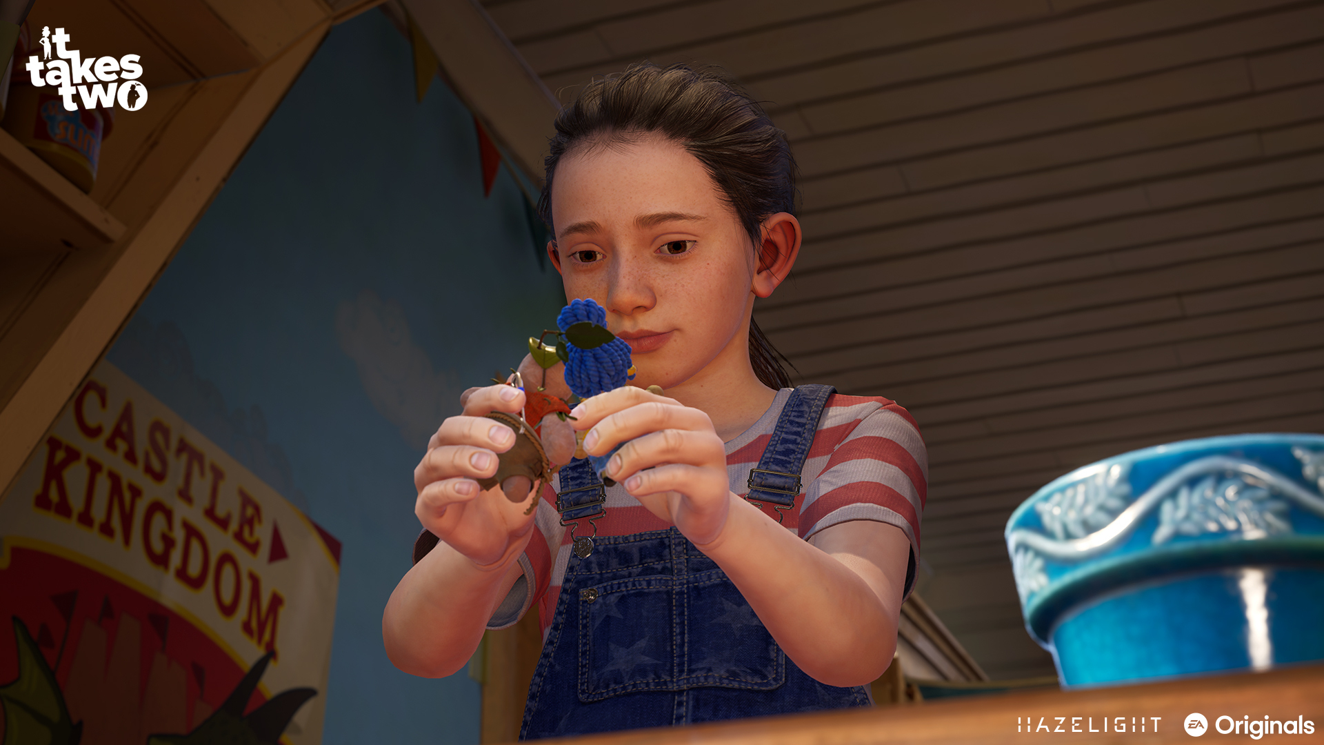 Dziewczynka patrzy na niebiesko-białą zabawkę w pokoju. Tytuł gry 'It Takes Two' widoczny w lewym górnym rogu.