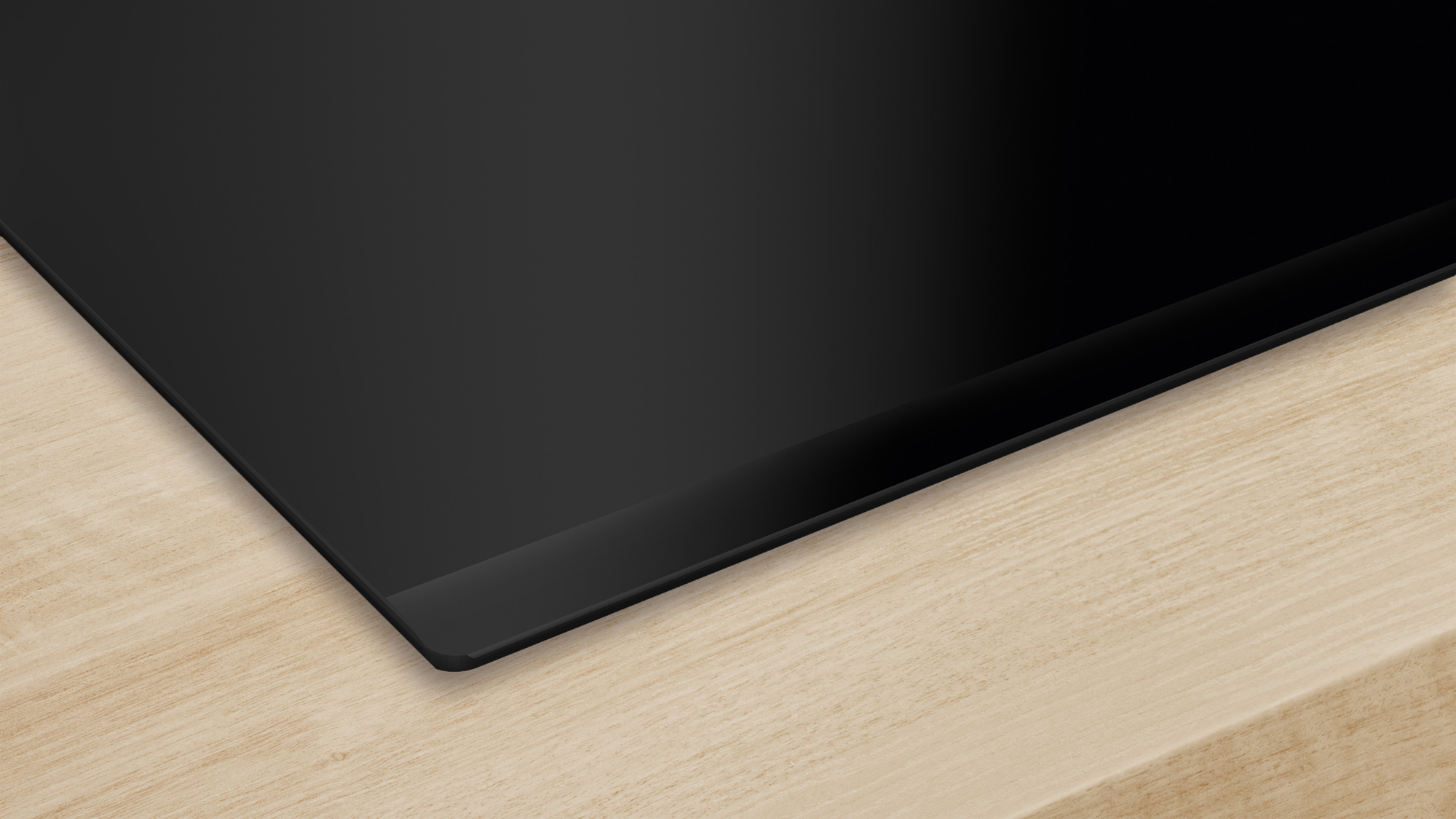 Piano cottura nero su superficie in legno chiaro, con bordo smussato.