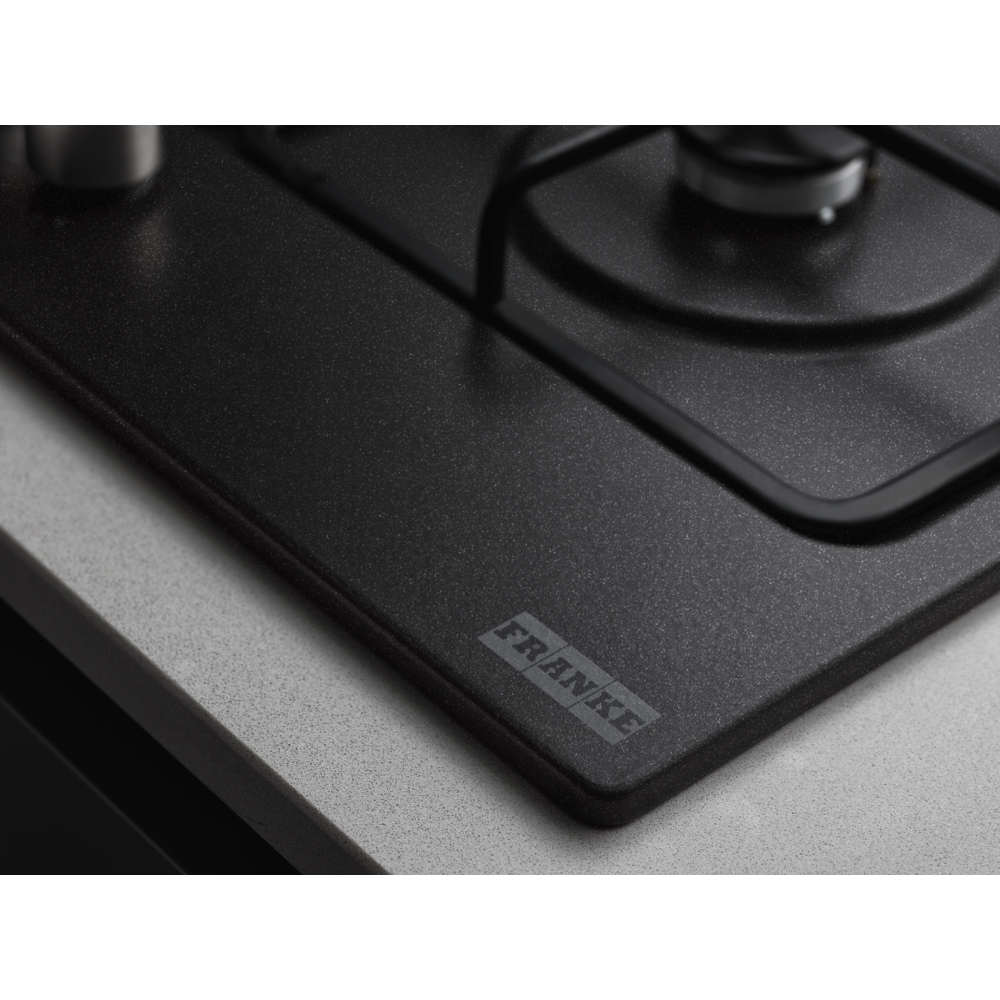 Primer plano de una placa de cocina negra con el logo 'FRANKE'. Encimera gris, superficie negra.
