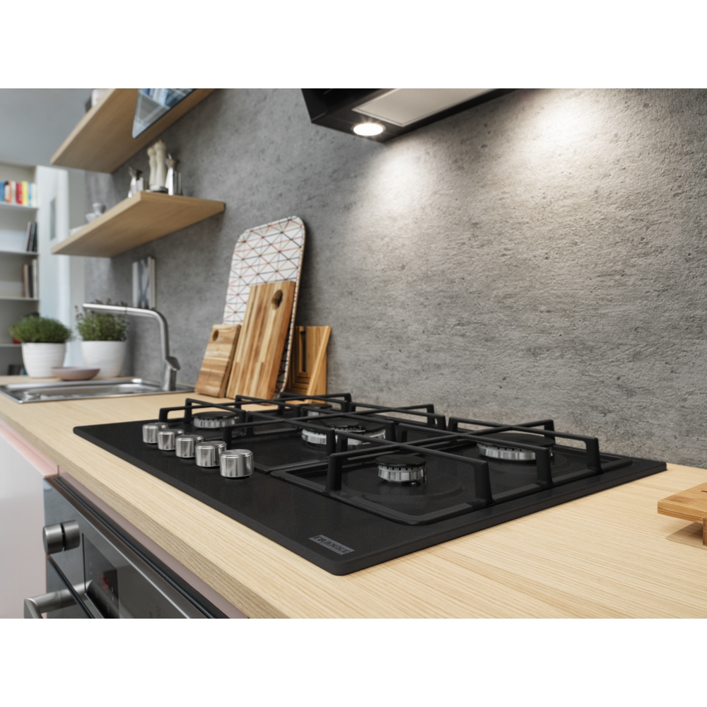 Placa de gas negra sobre encimera de madera. Mandos giratorios plateados. Cocina con estantes y fregadero.