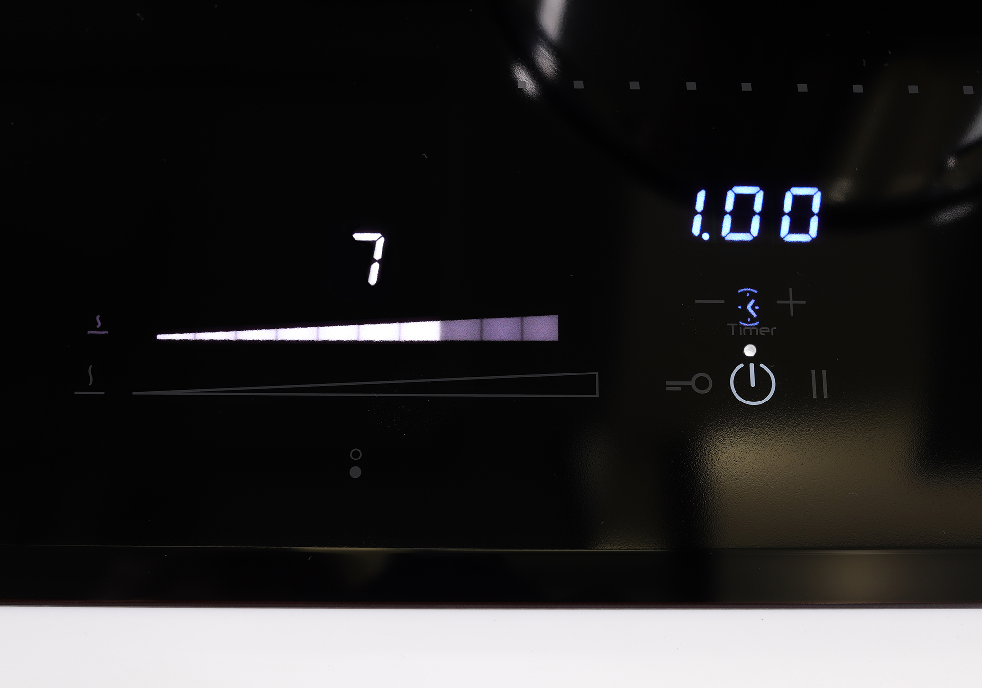 Close-up of a black hob control panel. Displays a number 7 and a timer with a power button.
