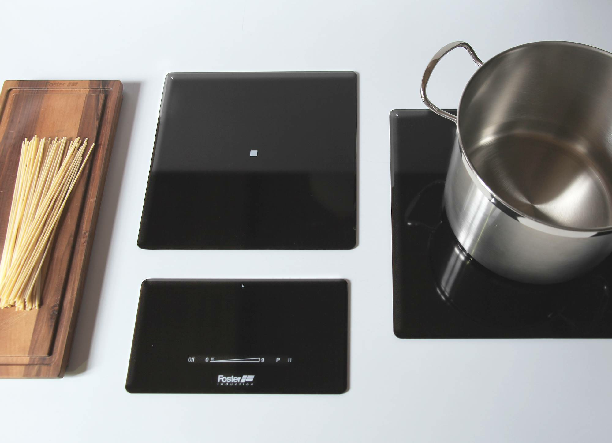 Scena cucina. Piano cottura con pentola, pasta e tagliere su superficie bianca.