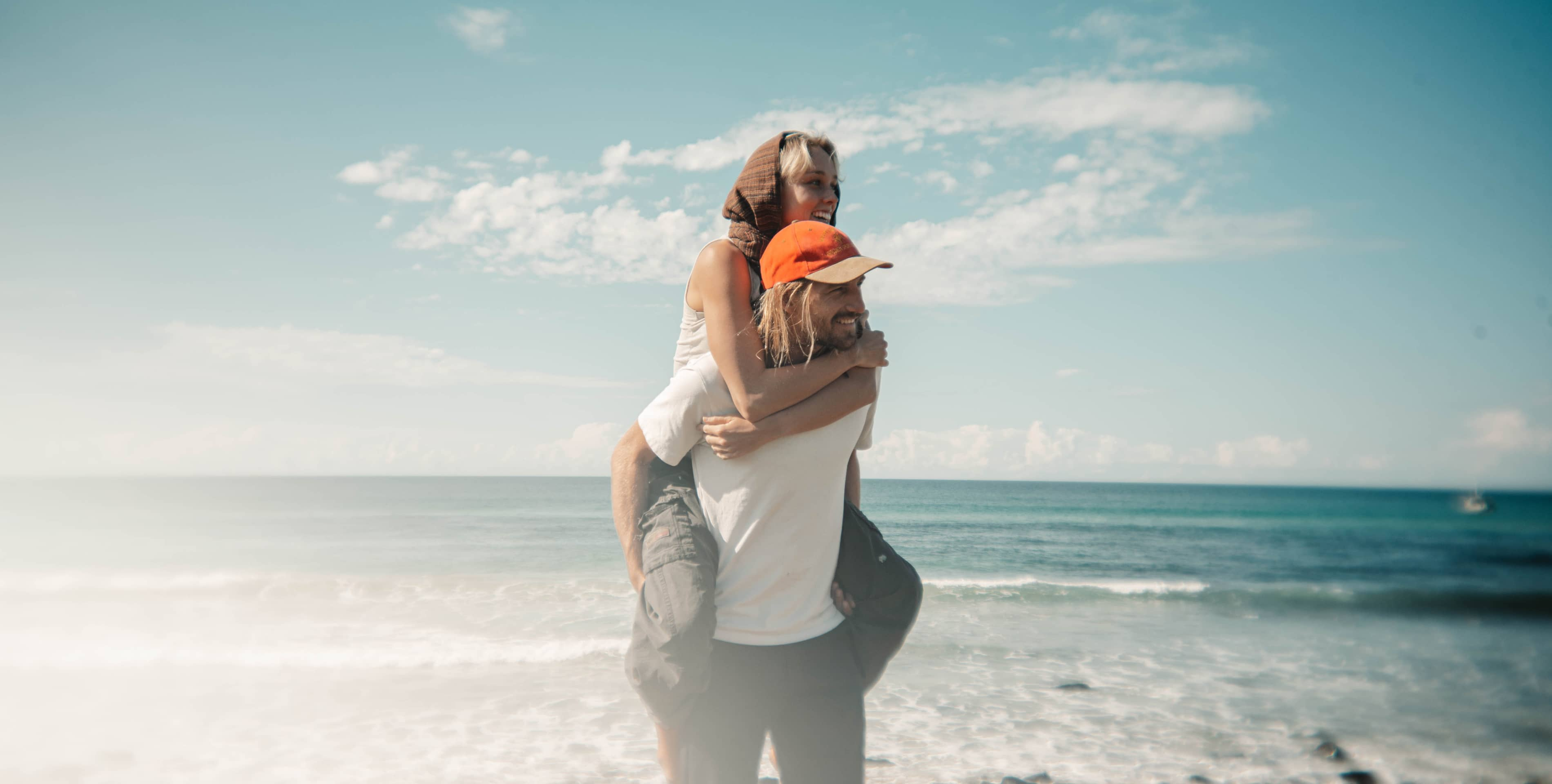 Para, mężczyzna nosi kobietę na barana na plaży.