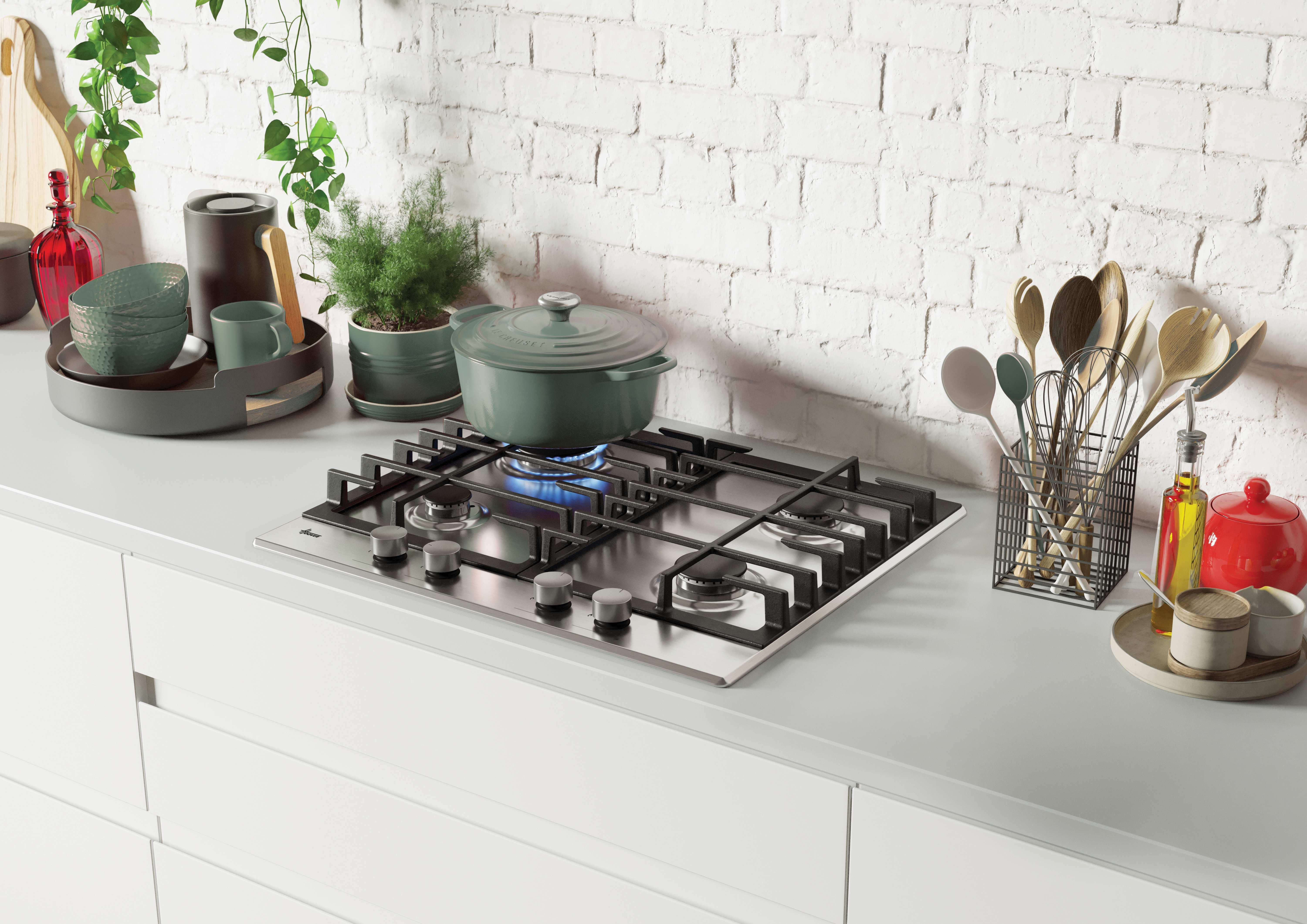 Encimera de cocina con placa de gas, olla, utensilios y accesorios. Pared de ladrillo blanco al fondo.