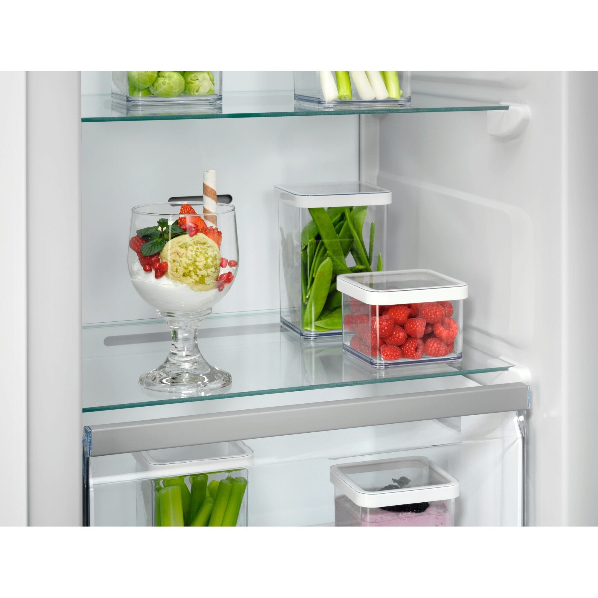 Interior de frigorífico con estantes de cristal con recipientes de comida y una copa de postre elegante.