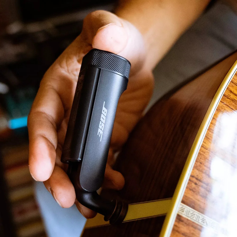 Mano che tiene un trasmettitore audio nero vicino a una chitarra.