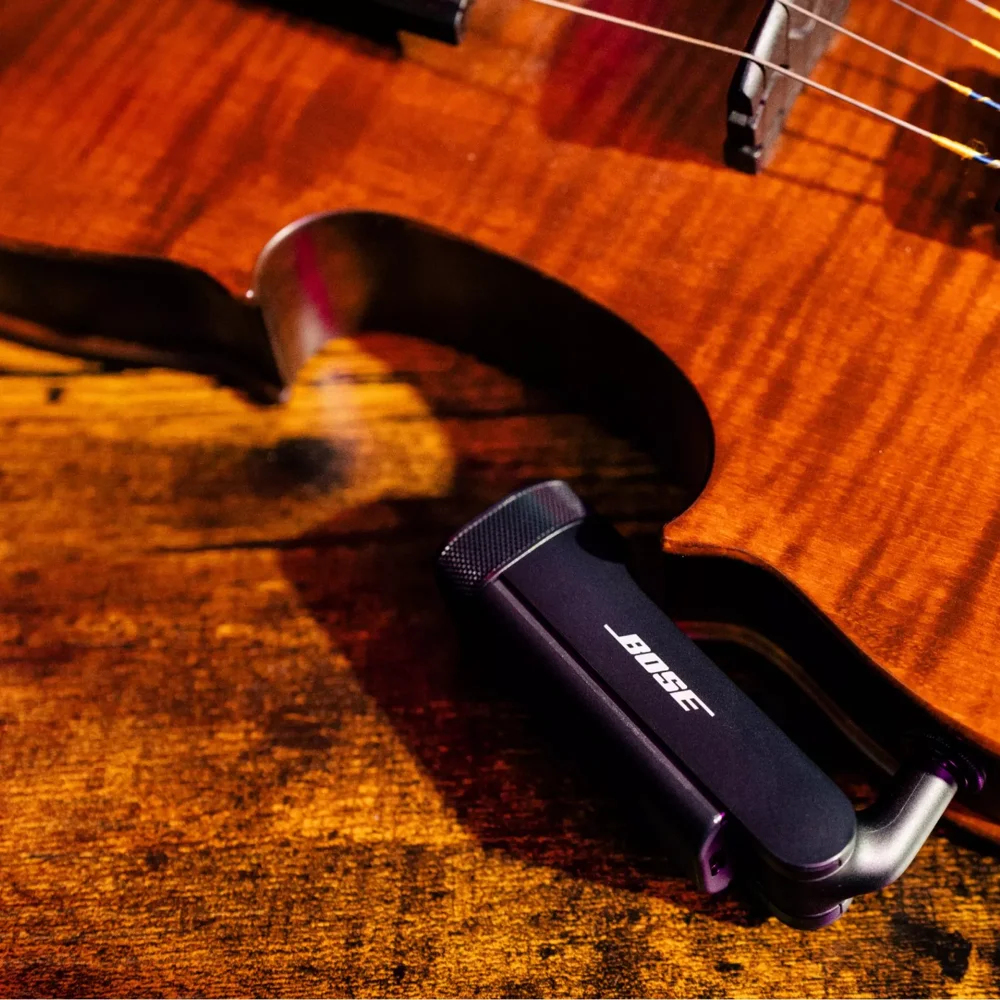 Trasmettitore audio nero vicino al corpo di una chitarra in legno.