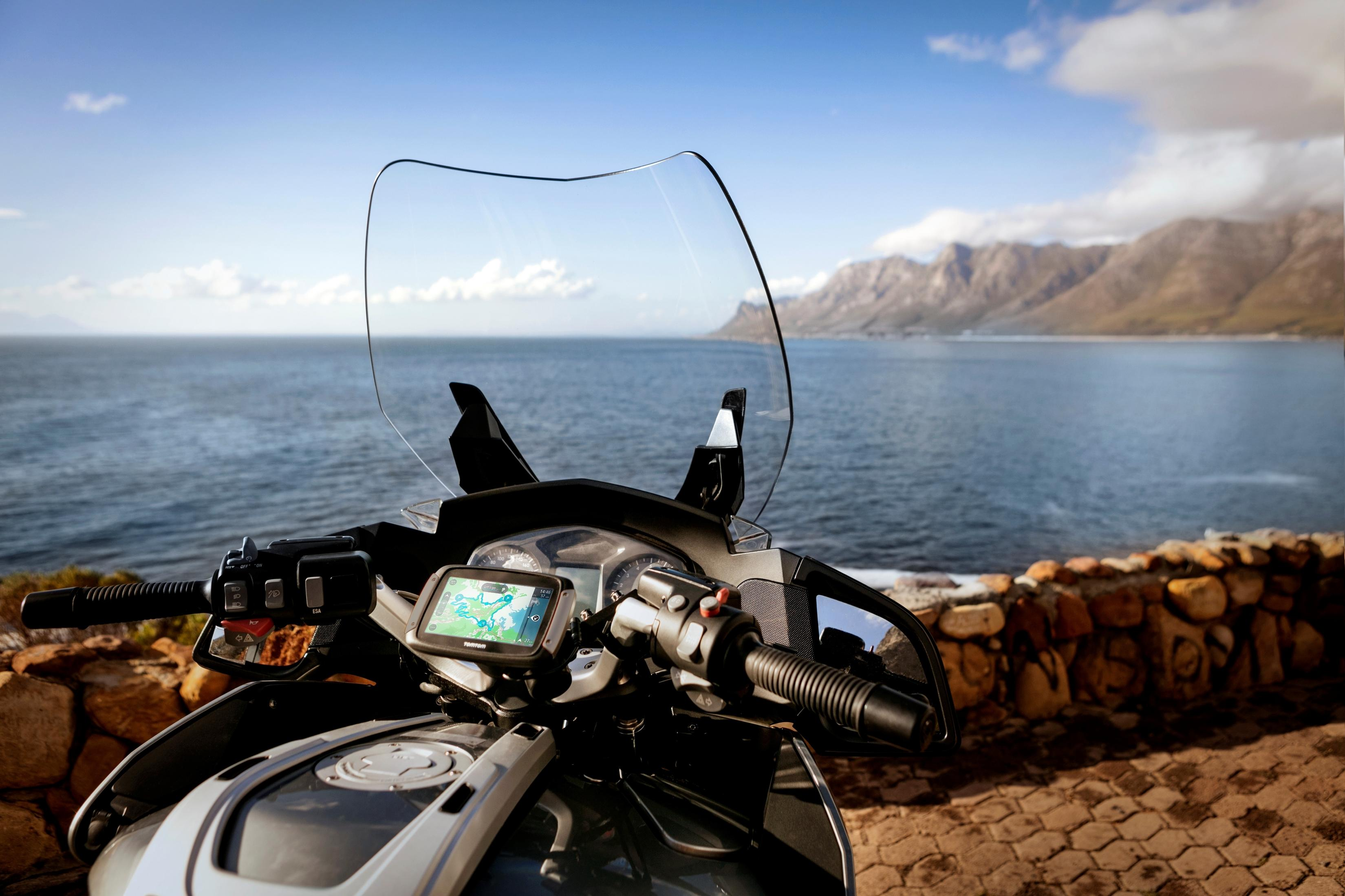 Motorrad auf einer Straße mit malerischer Aussicht auf das Meer und die Berge im Hintergrund.