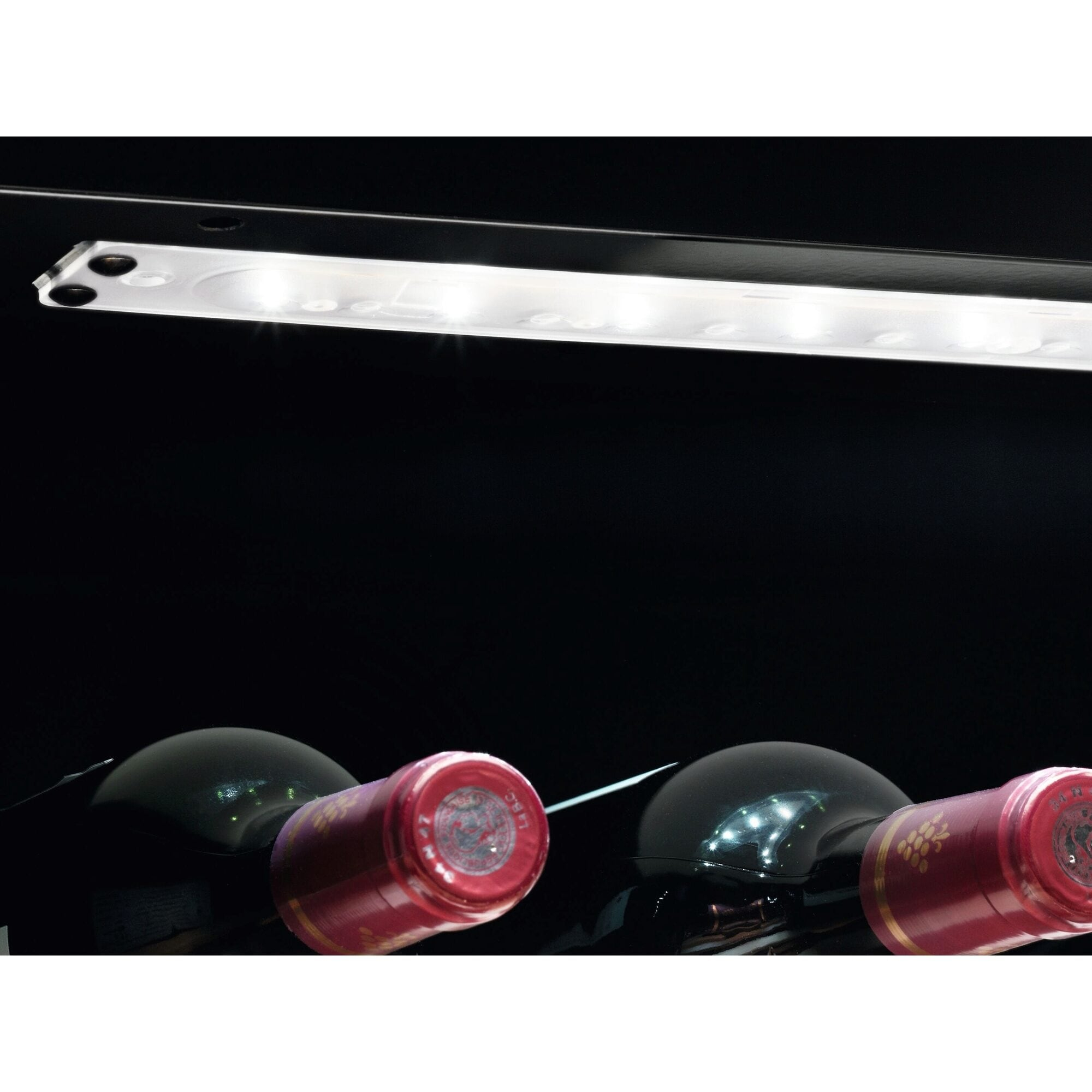 Botellas de vino con tapas rojas y una luz superior en una nevera de vino negra.