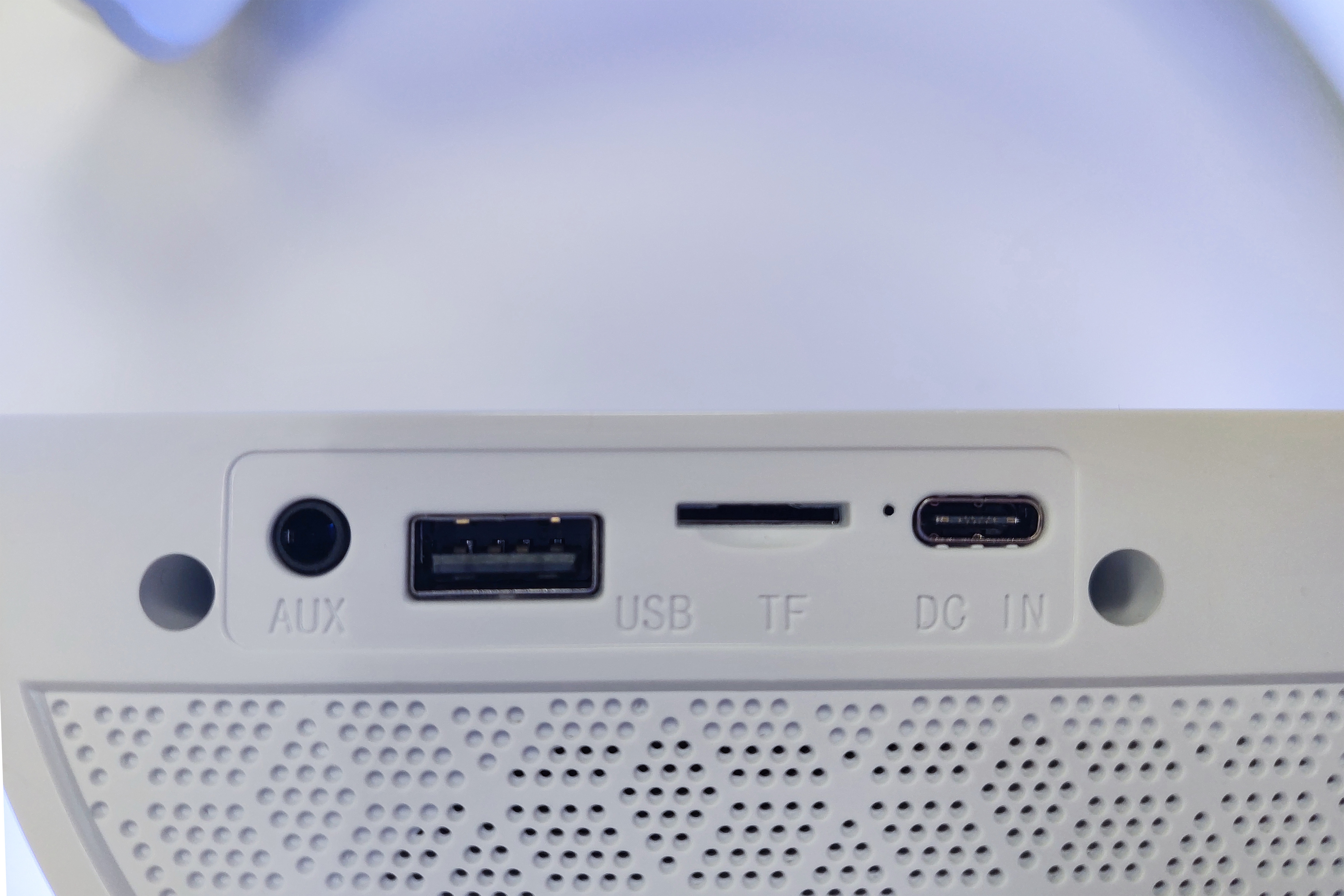 Un altoparlante bianco con porte. AUX, USB, TF e DC IN sono etichettati. È visibile anche una porta di ricarica.