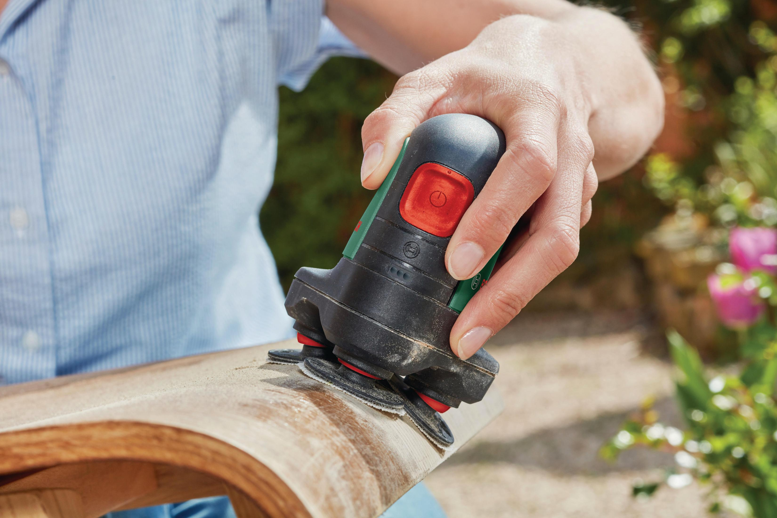 Une main utilise un outil électrique pour poncer une surface en bois incurvée.