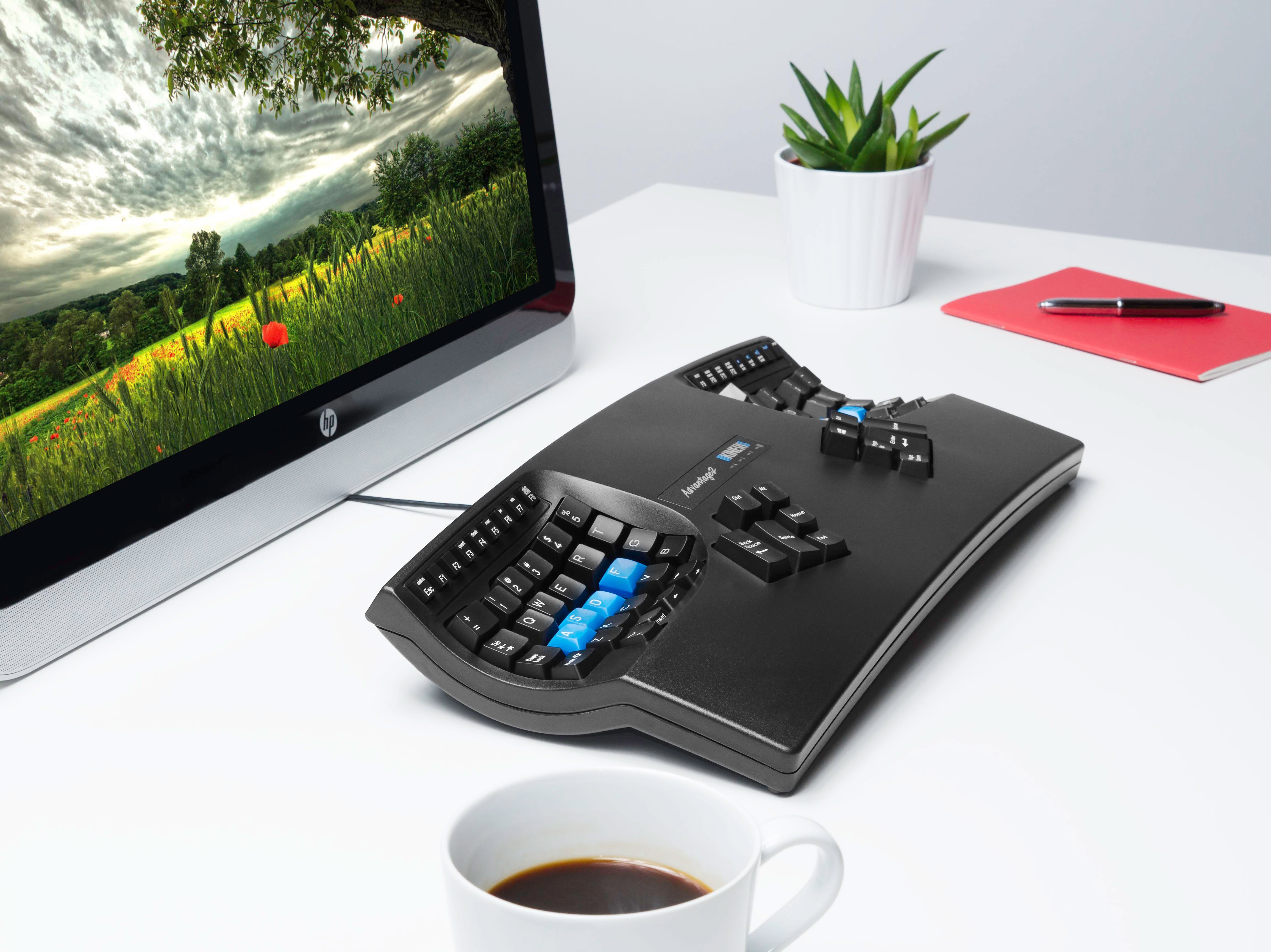 Tastiera ergonomica su scrivania bianca con monitor e tazza di caffè.