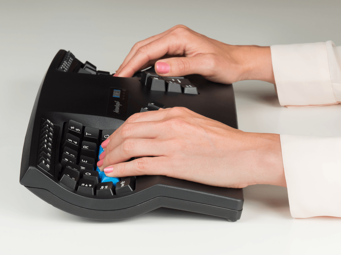 Mani che digitano su tastiera ergonomica nera. Smalto rosa visibile.