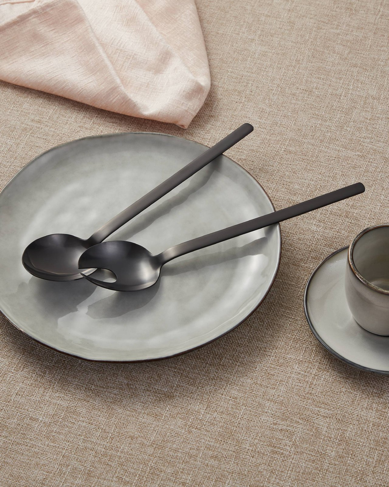 Posate da insalata su un piatto, con tazza e tovagliolo, su tovaglia beige.