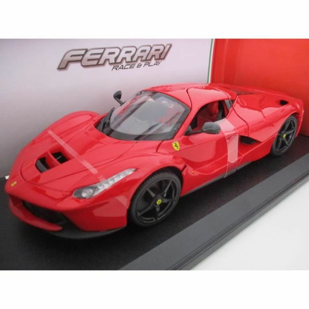Czerwony model samochodu Ferrari, czarne koła, na czarnej powierzchni, z logo Ferrari.