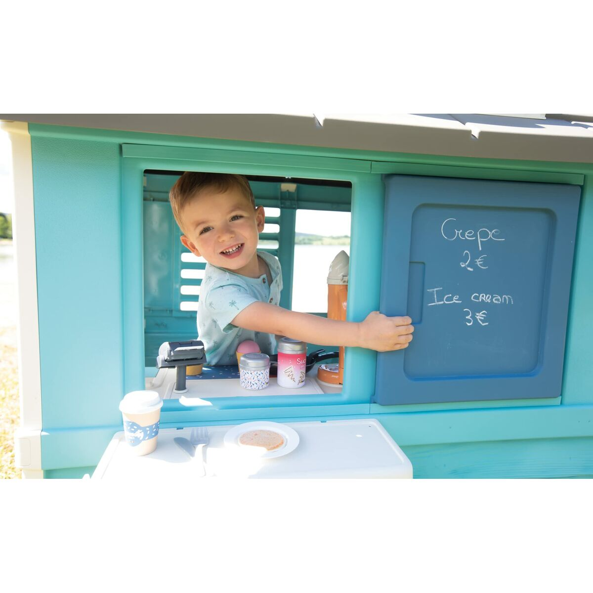Niño sonríe en ventana de casita, mostrando menú de crepes y helado.