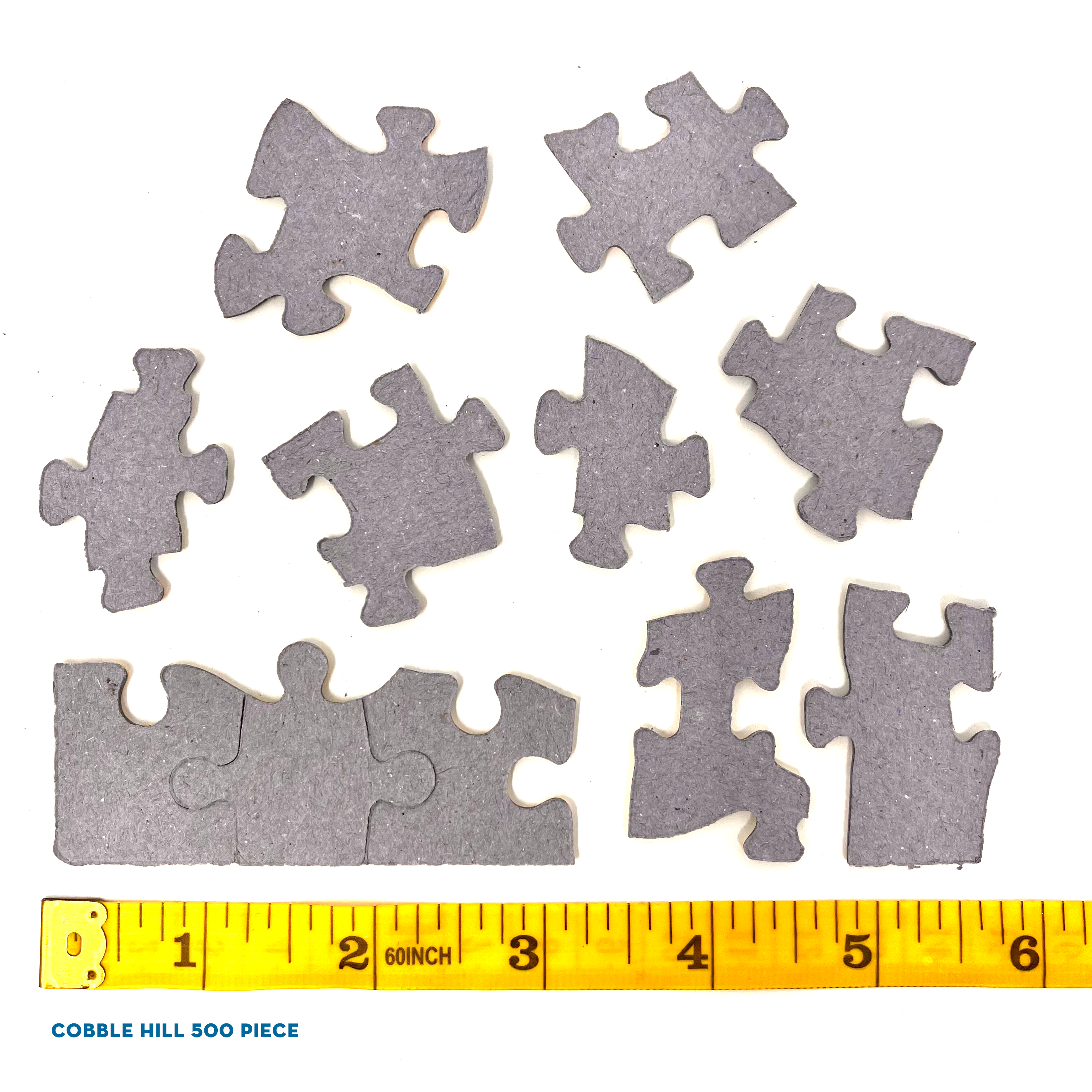 Puzzleteile und ein Lineal liegen auf einer weißen Oberfläche. Die Puzzleteile sind grau.