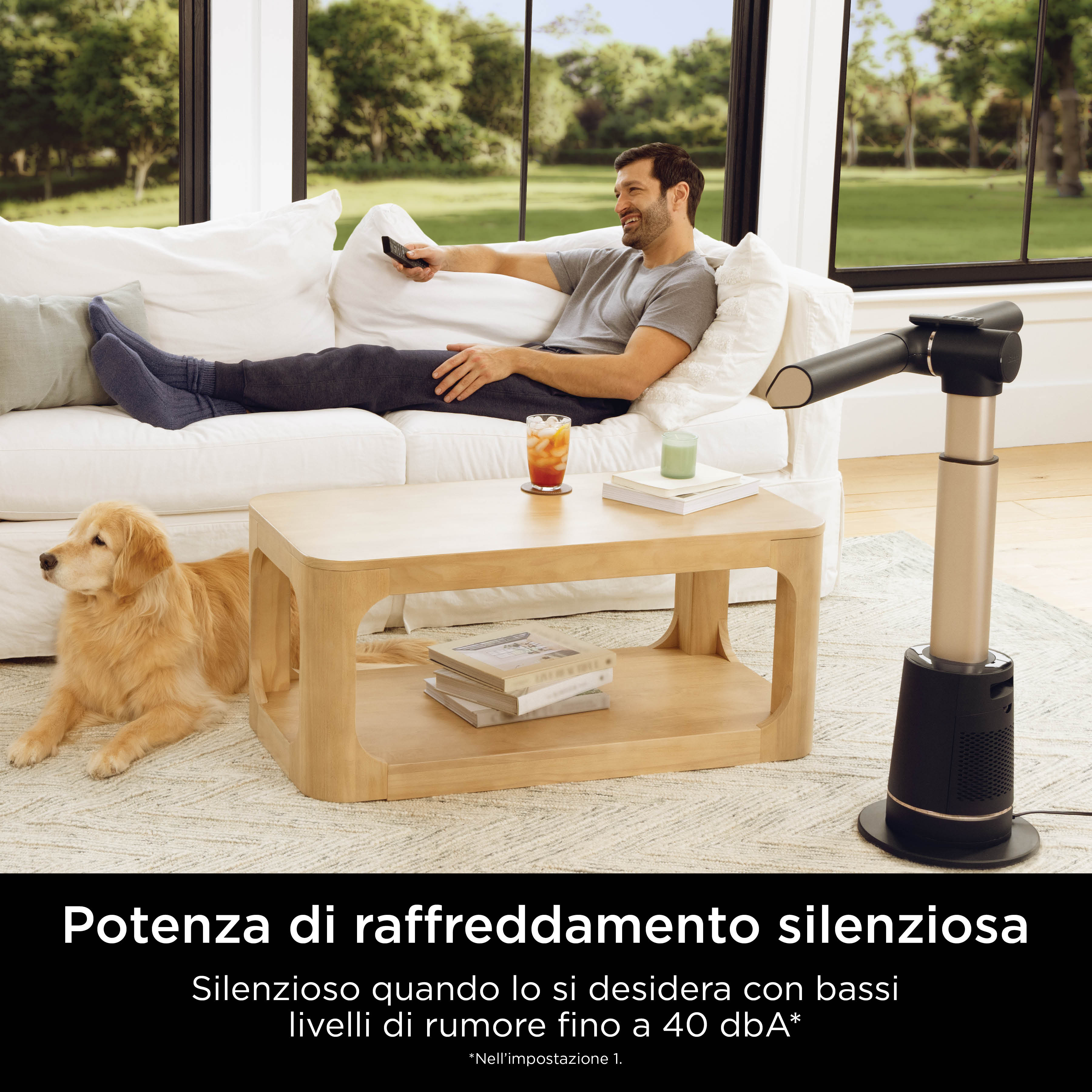 Mężczyzna leży na białej kanapie z psem. Stół z przedmiotami i wentylator Shark znajdują się w pobliżu.