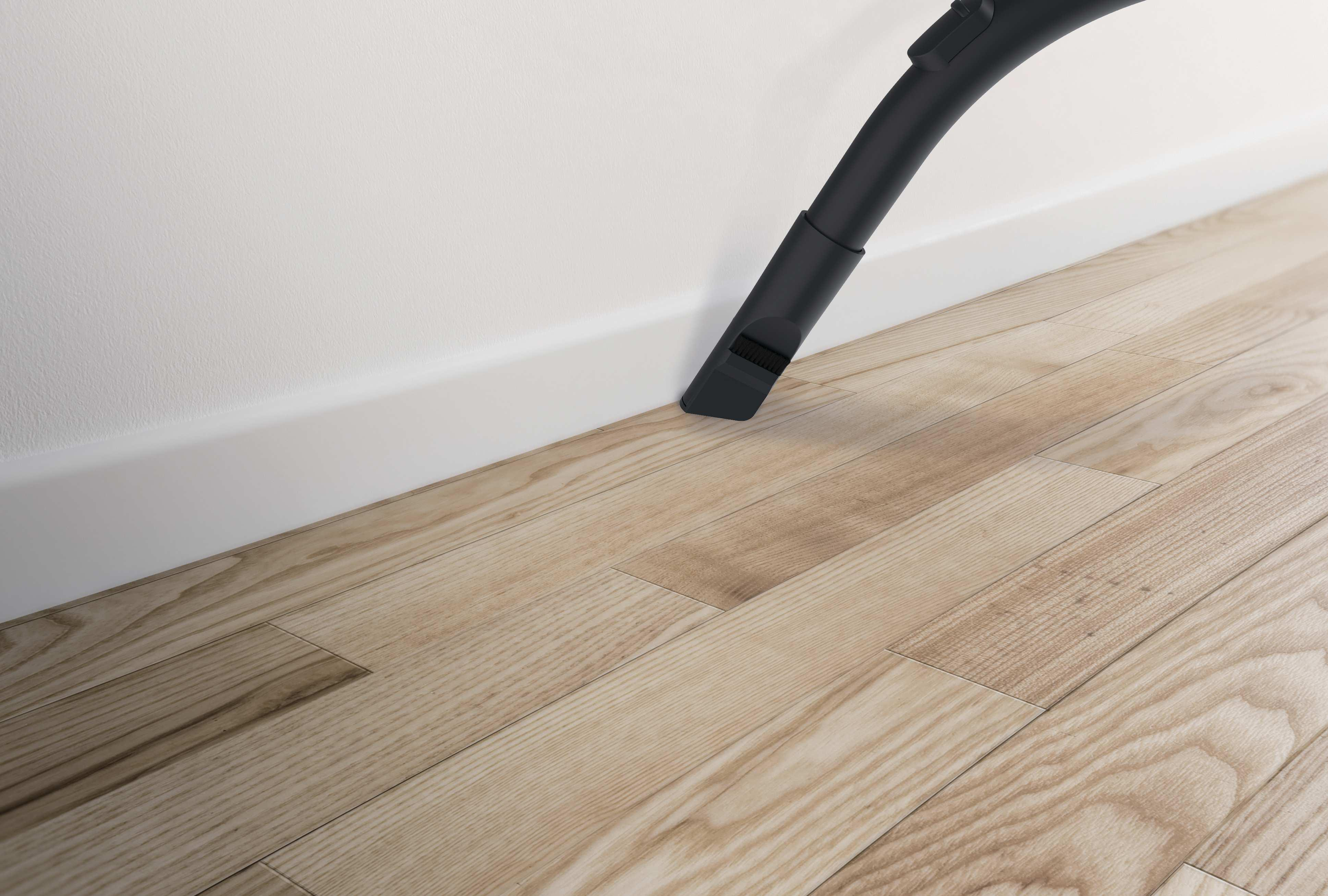 Dysza odkurzacza czyści drewnianą podłogę obok białej ściany i listwy przypodłogowej.