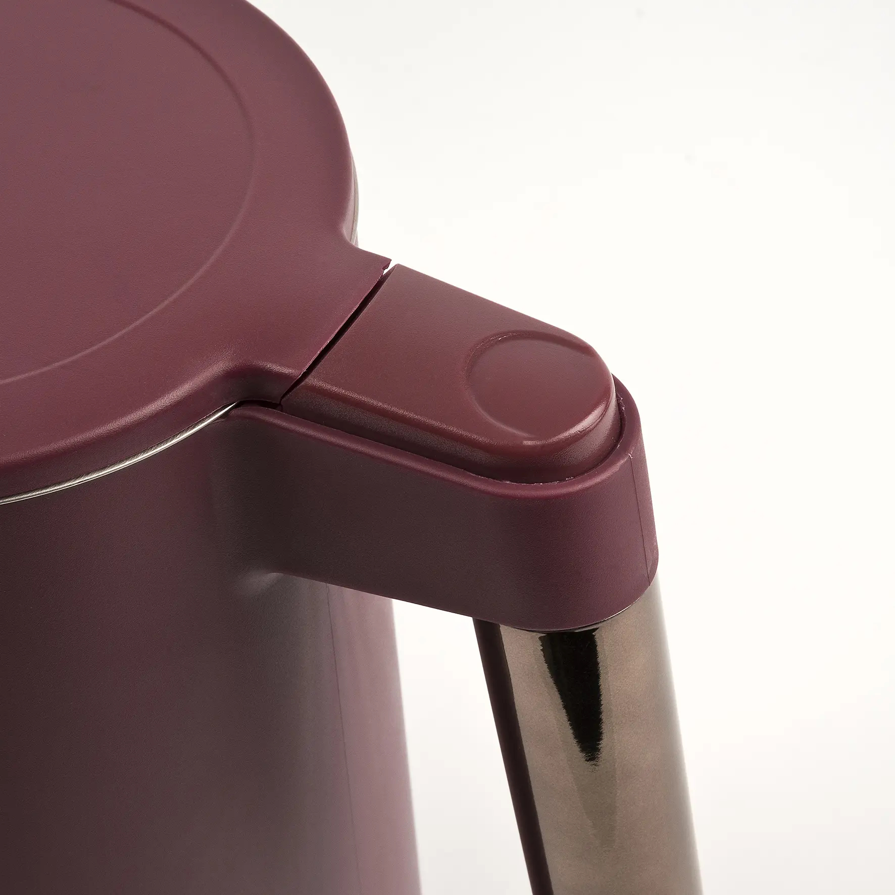 Zbliżenie pokrywy i uchwytu bordowego czajnika, pokazujące metal i plastik.