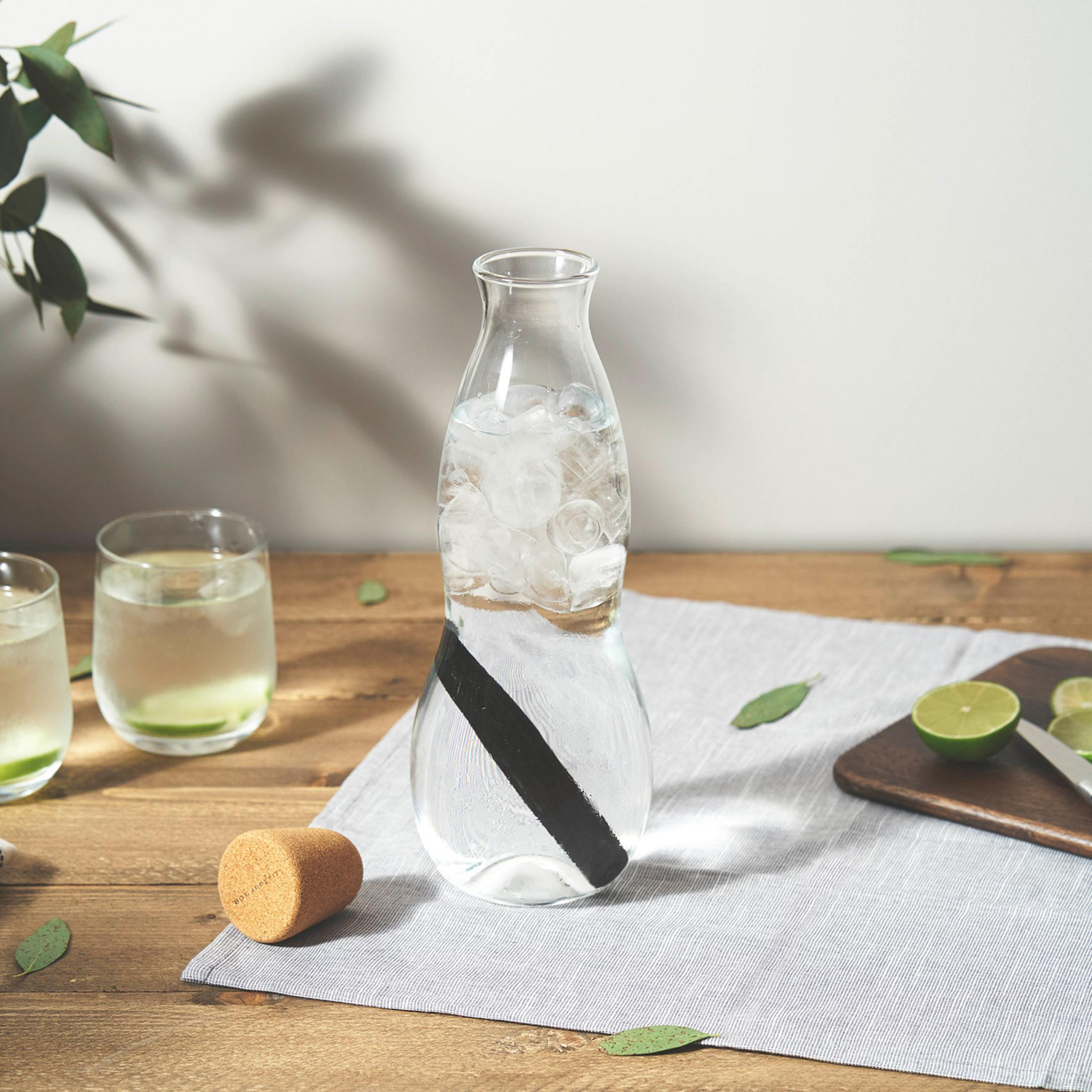 Glaswasserflasche mit Eis, schwarzem Stab und Korken. Zwei Gläser mit Wasser und Limette. Holztisch.
